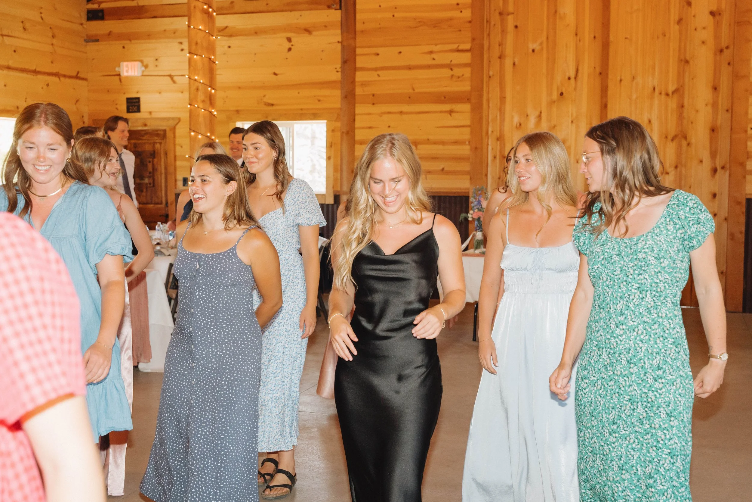 A group of young women dancing and enjoying themselves at an indoor event in a wooden hall.