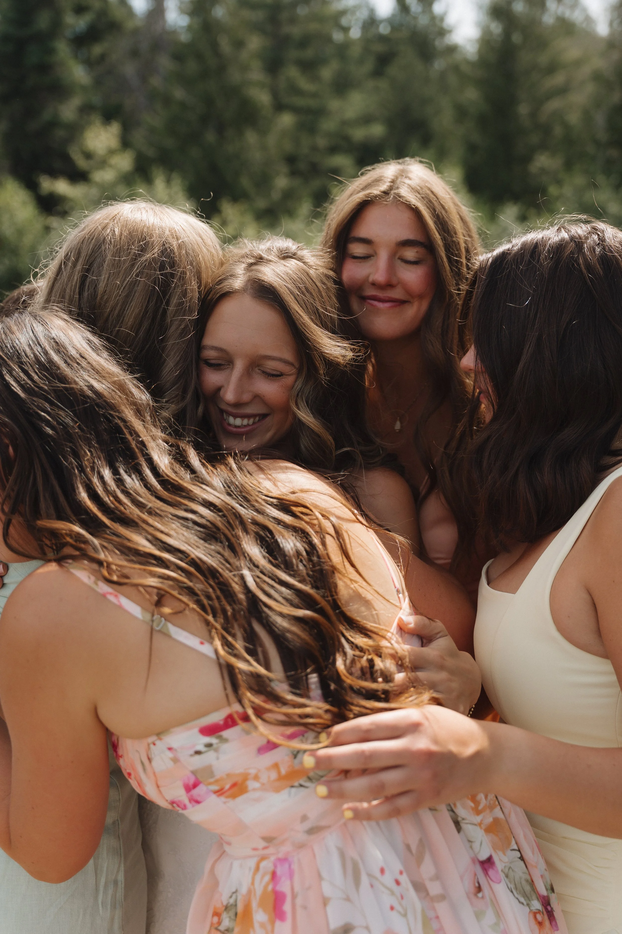 A group of women embracing outdoors on a sunny day, smiling and hugging each other in a joyful moment.