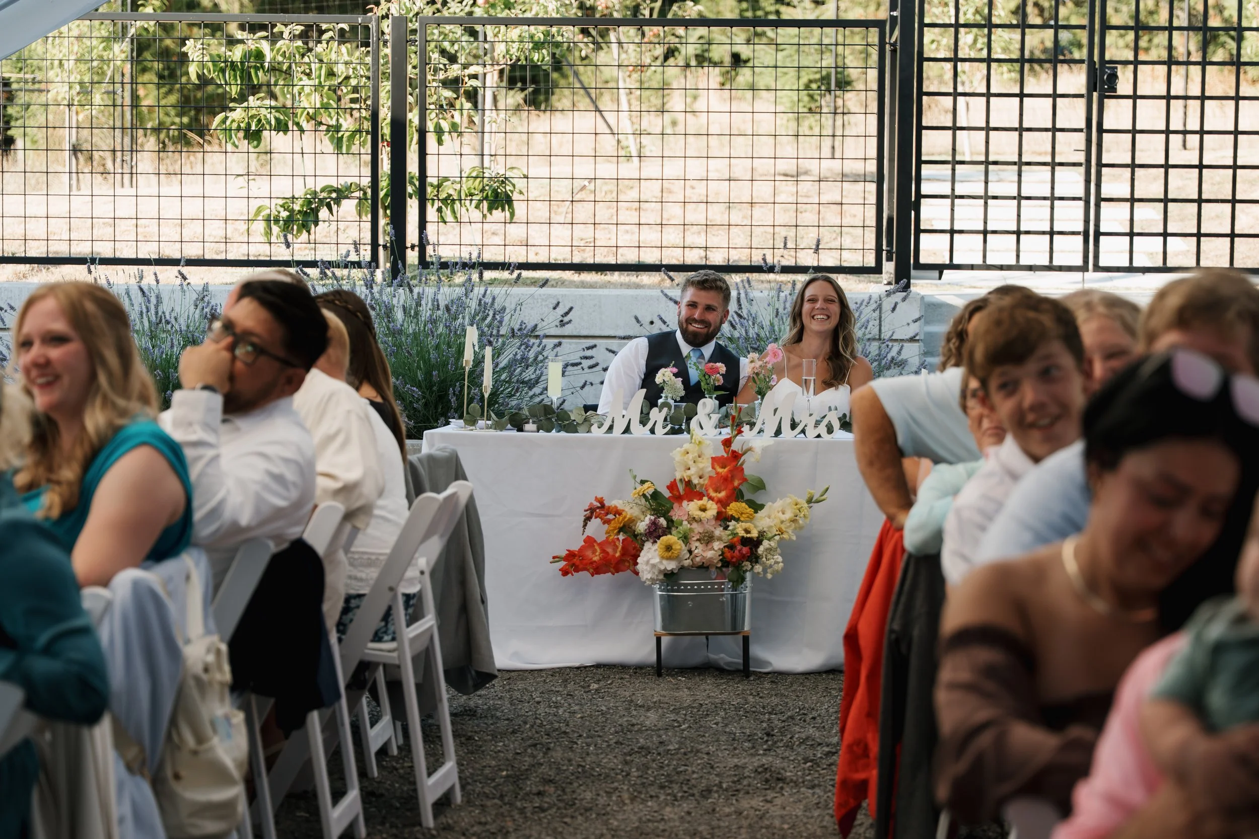 A wedding reception with a happy bride and groom sitting at a decorated table with a 