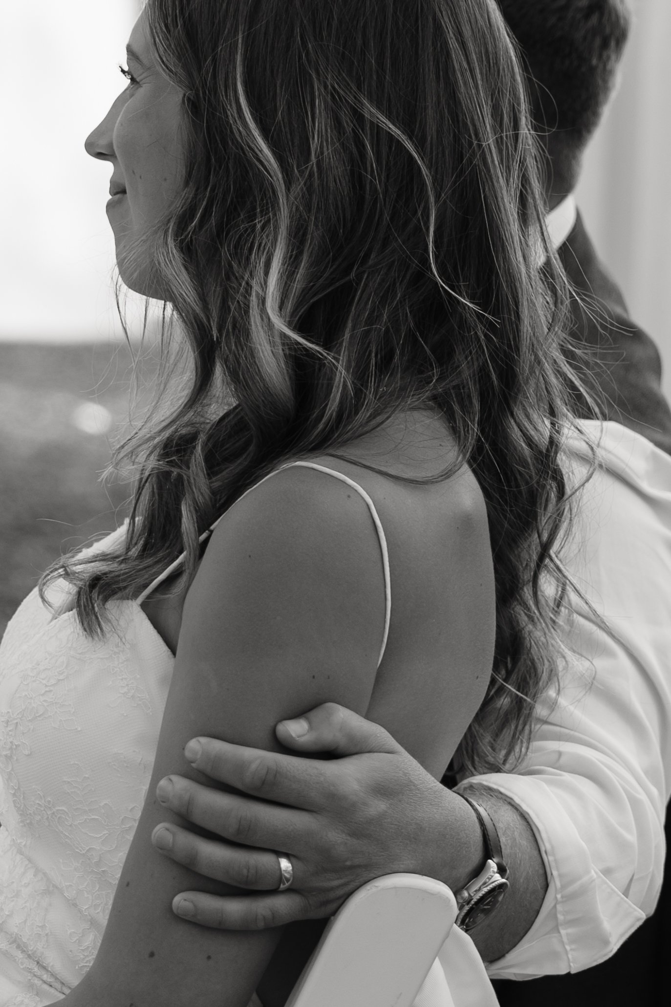 A woman with long, wavy hair smiling in profile, seated with her arms crossed, in a close-up black and white photograph.