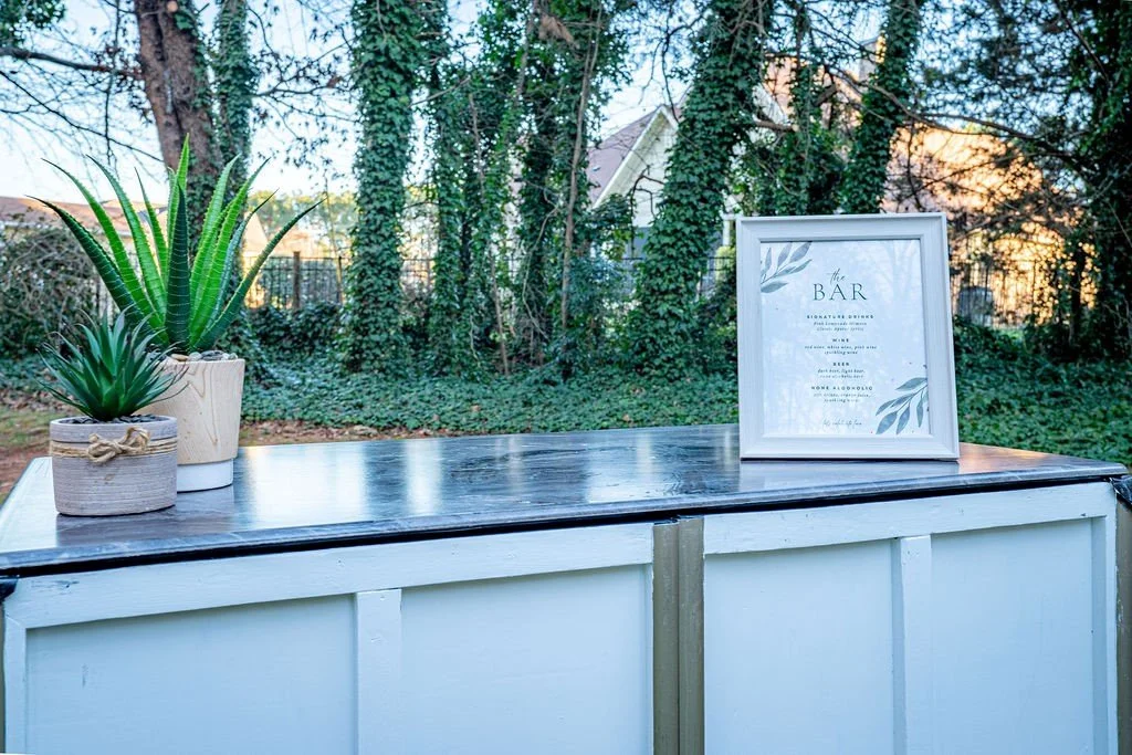 Outdoor bar setup with potted plants and a framed menu
