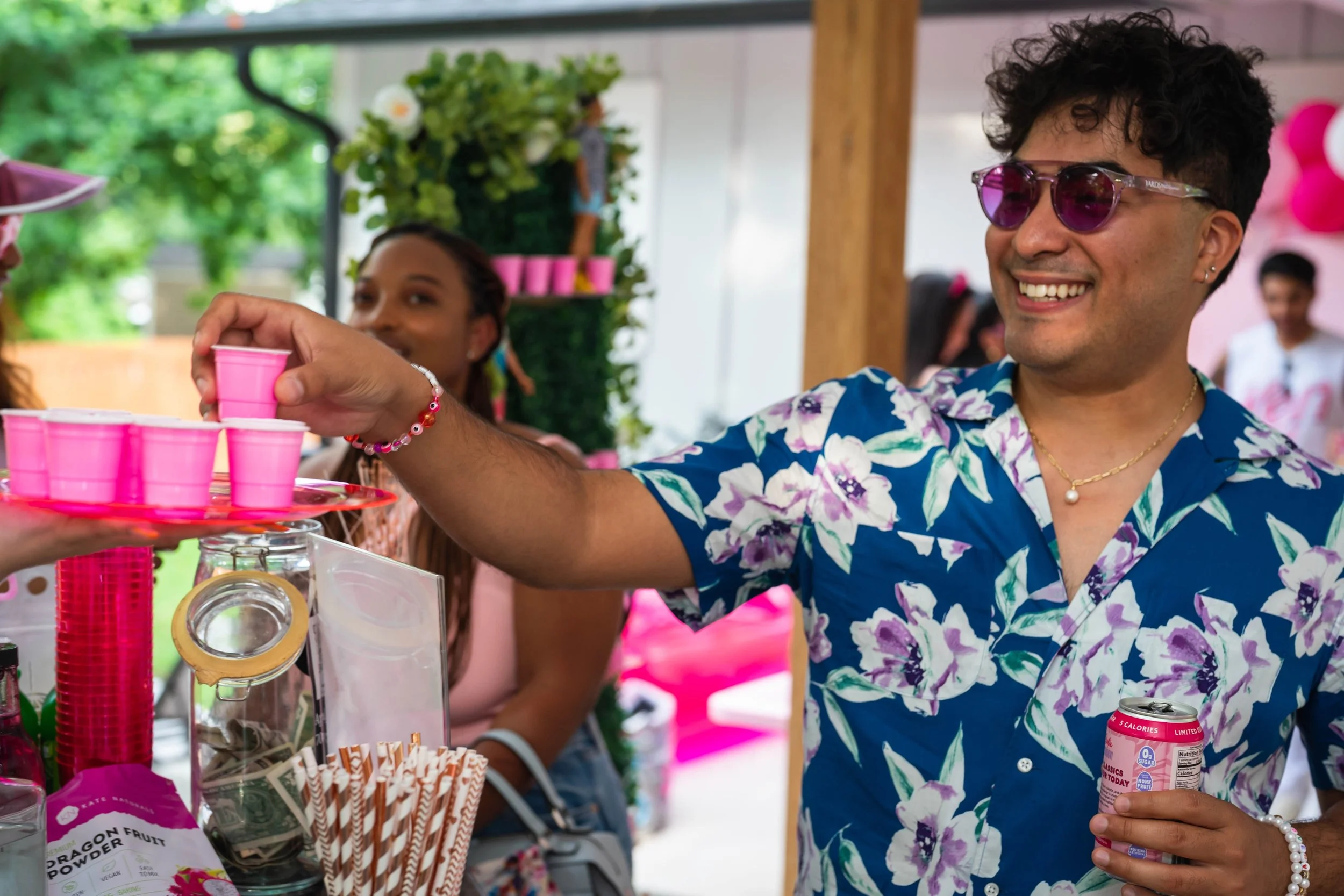 Person wearing floral shirt holding pink shot glass at a party