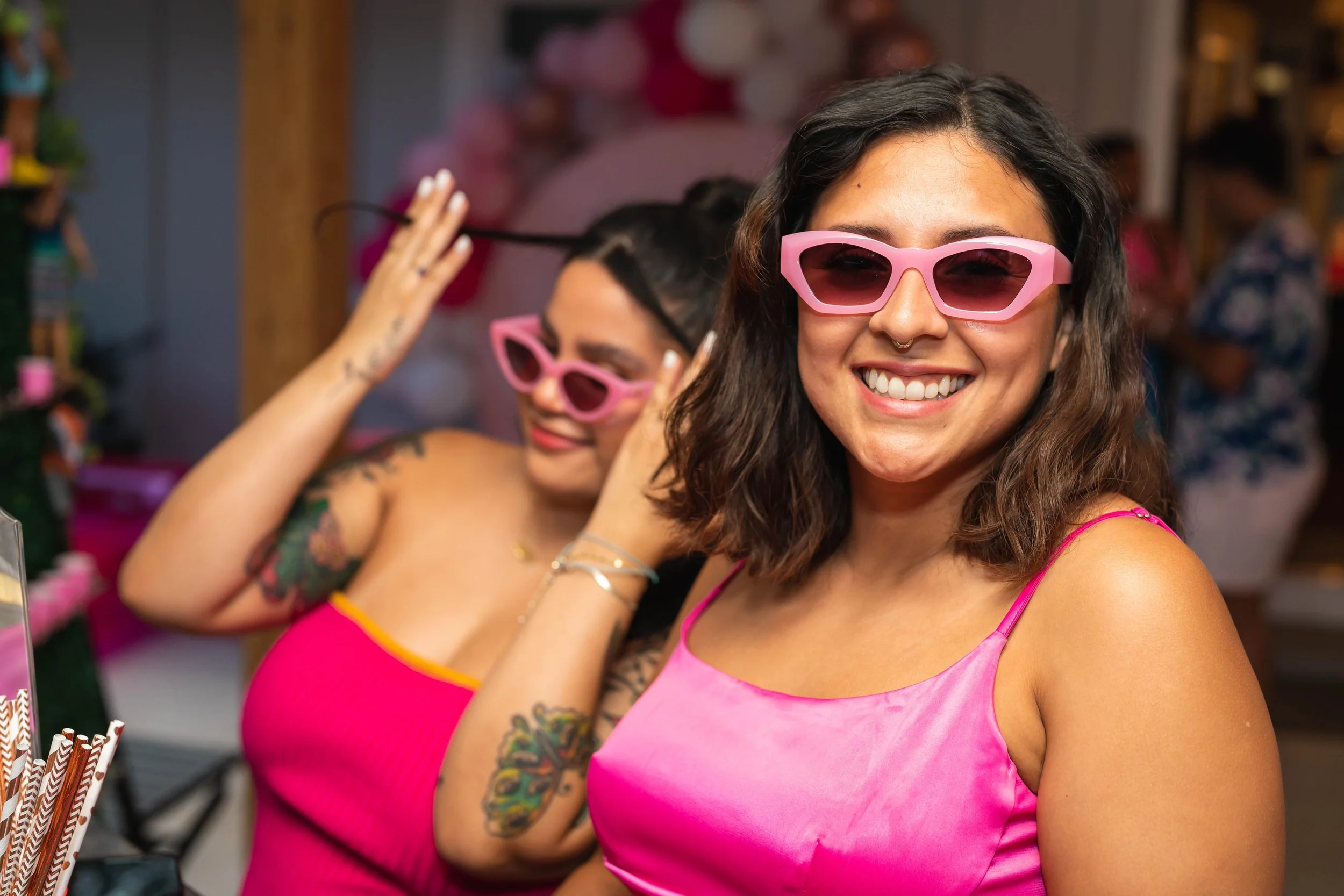 Two women wearing pink outfits and sunglasses, smiling at a party.