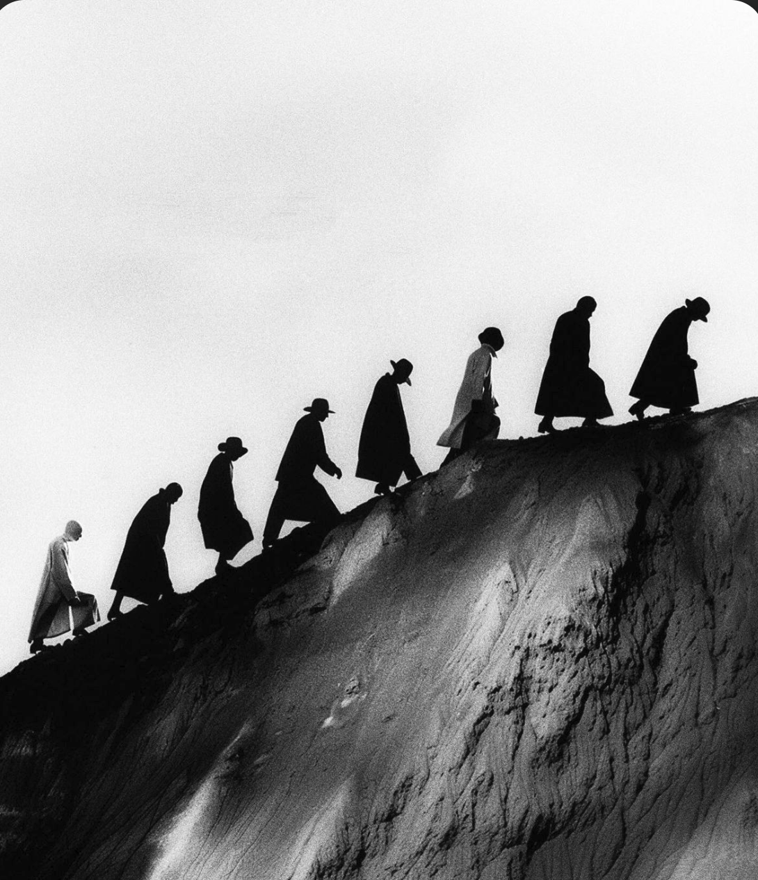 a line of people in a black and white landscape walking up a hill in a straight line. An interpretation of the word collaboration. 