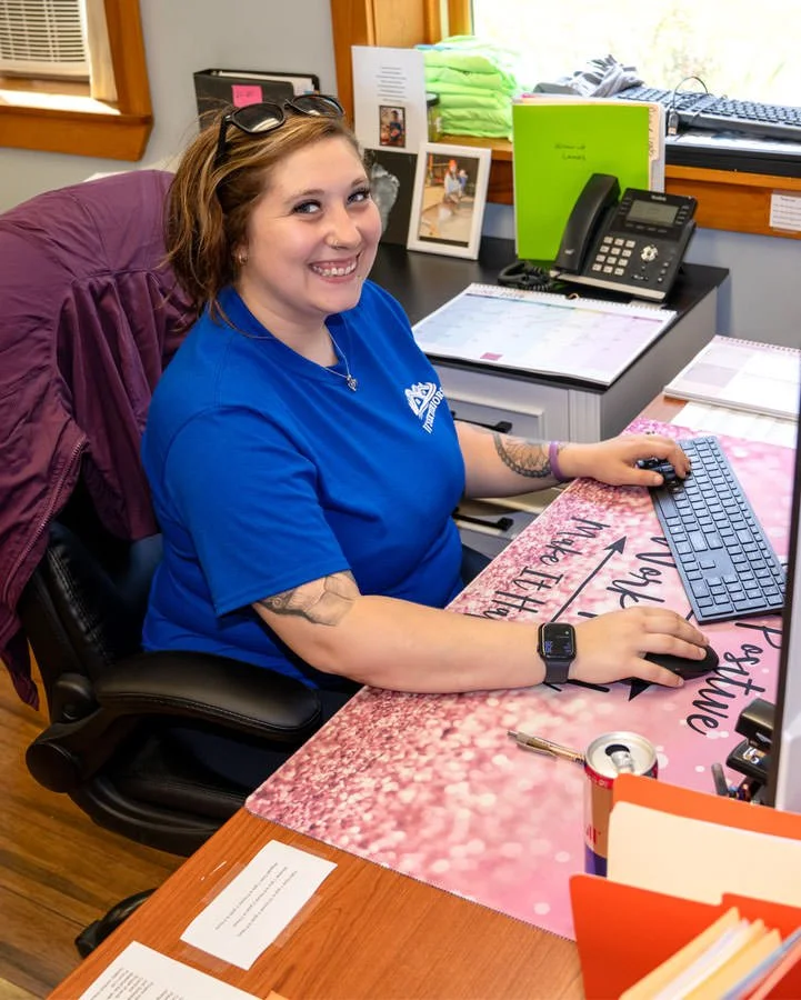 a female worker in a blue shirt smiling and using her keyboard in an office setting