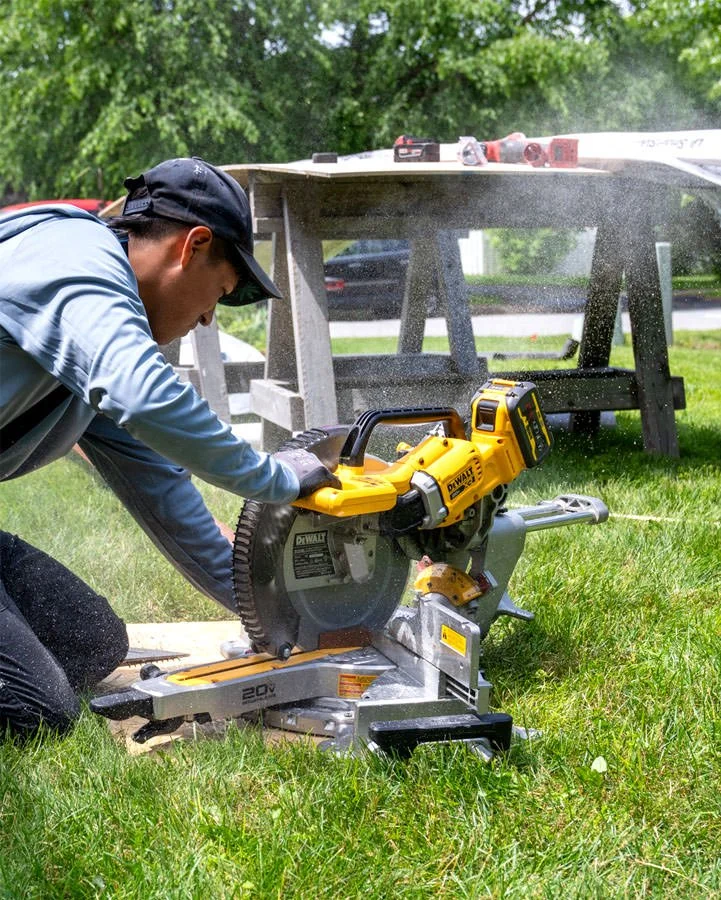 male worker cutting a section of board with a power saw outdoors on the grass