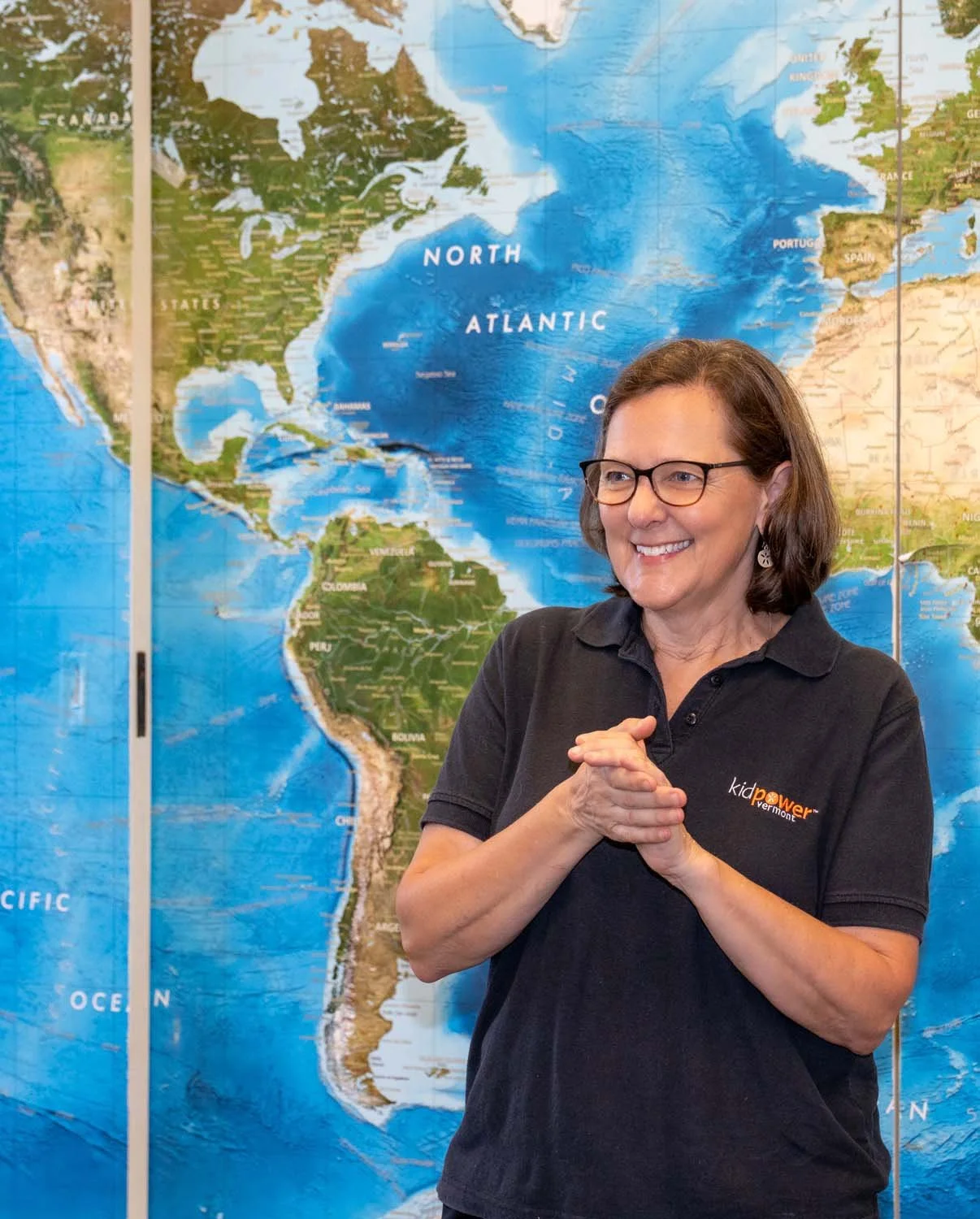 smiling woman standing in front of world map wearing a black polo shirt