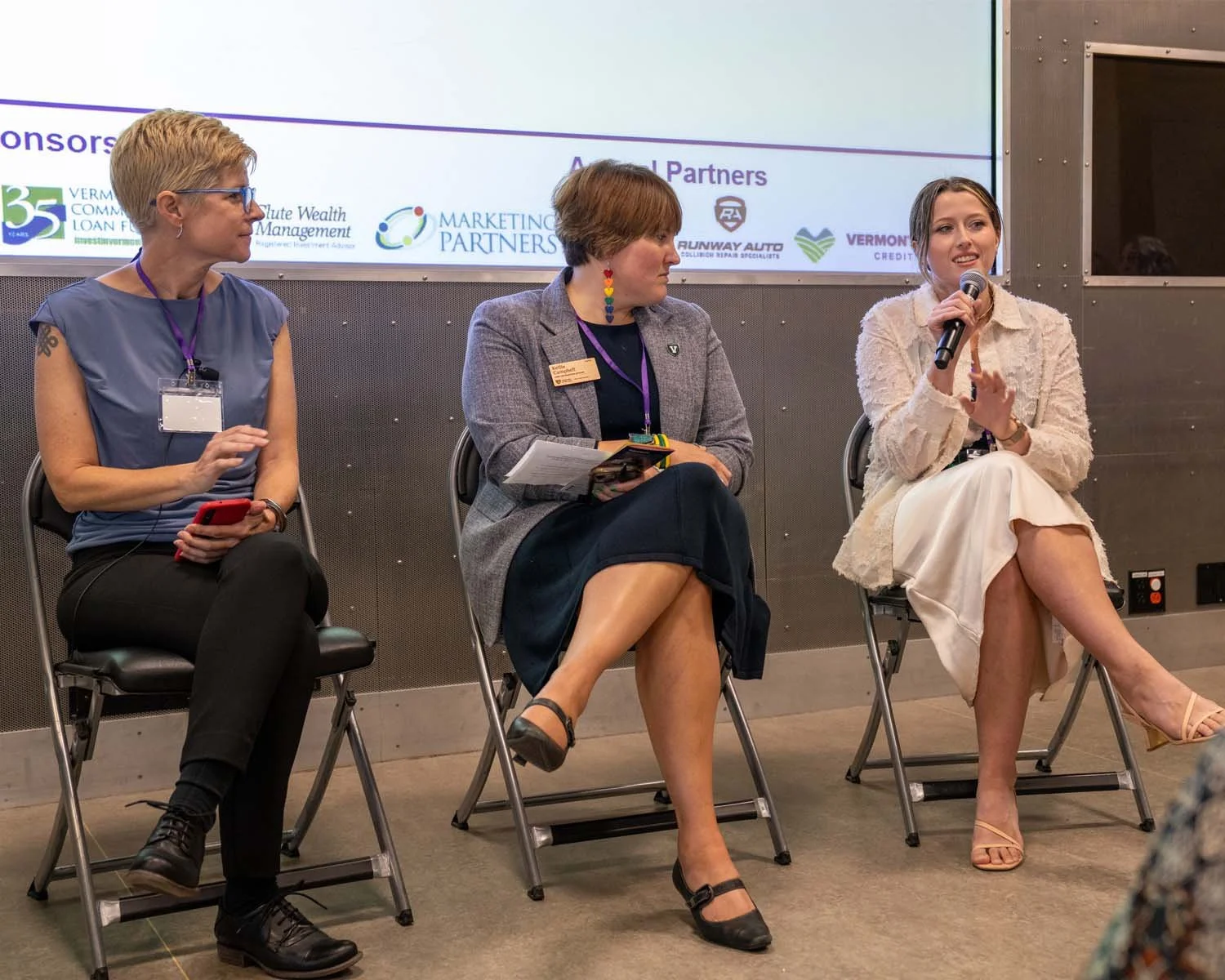 Three conference presenters are sitting on chairs discussing a topic