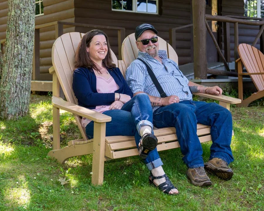 father and daughter sitting together on an outdoor seat in front of a log cabin