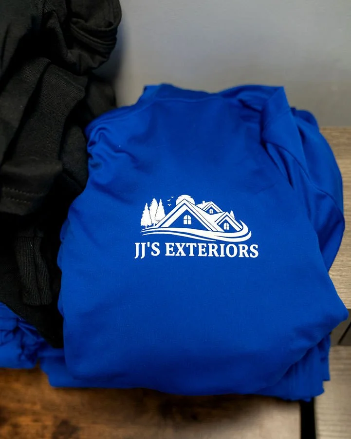 a pile of blue tshirts showing the logo of jj's exteriors