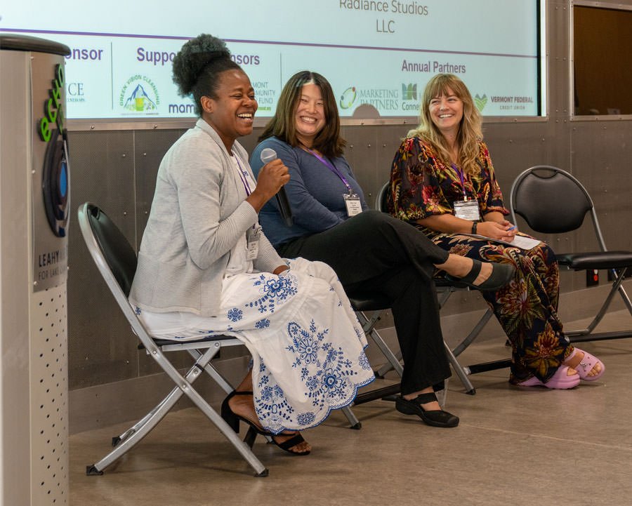 three speakers at a conference sitting in the stage area talking and laughing
