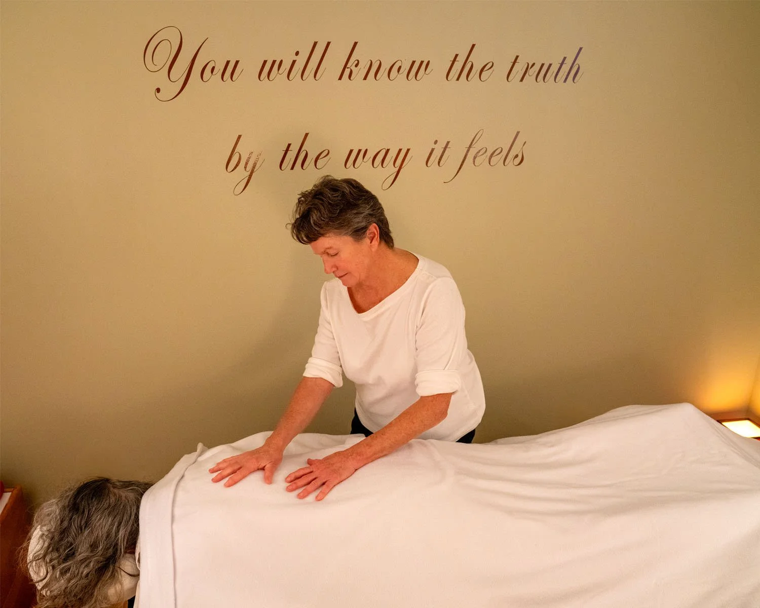 massage therapist placing her hands on the back of her client and looking down