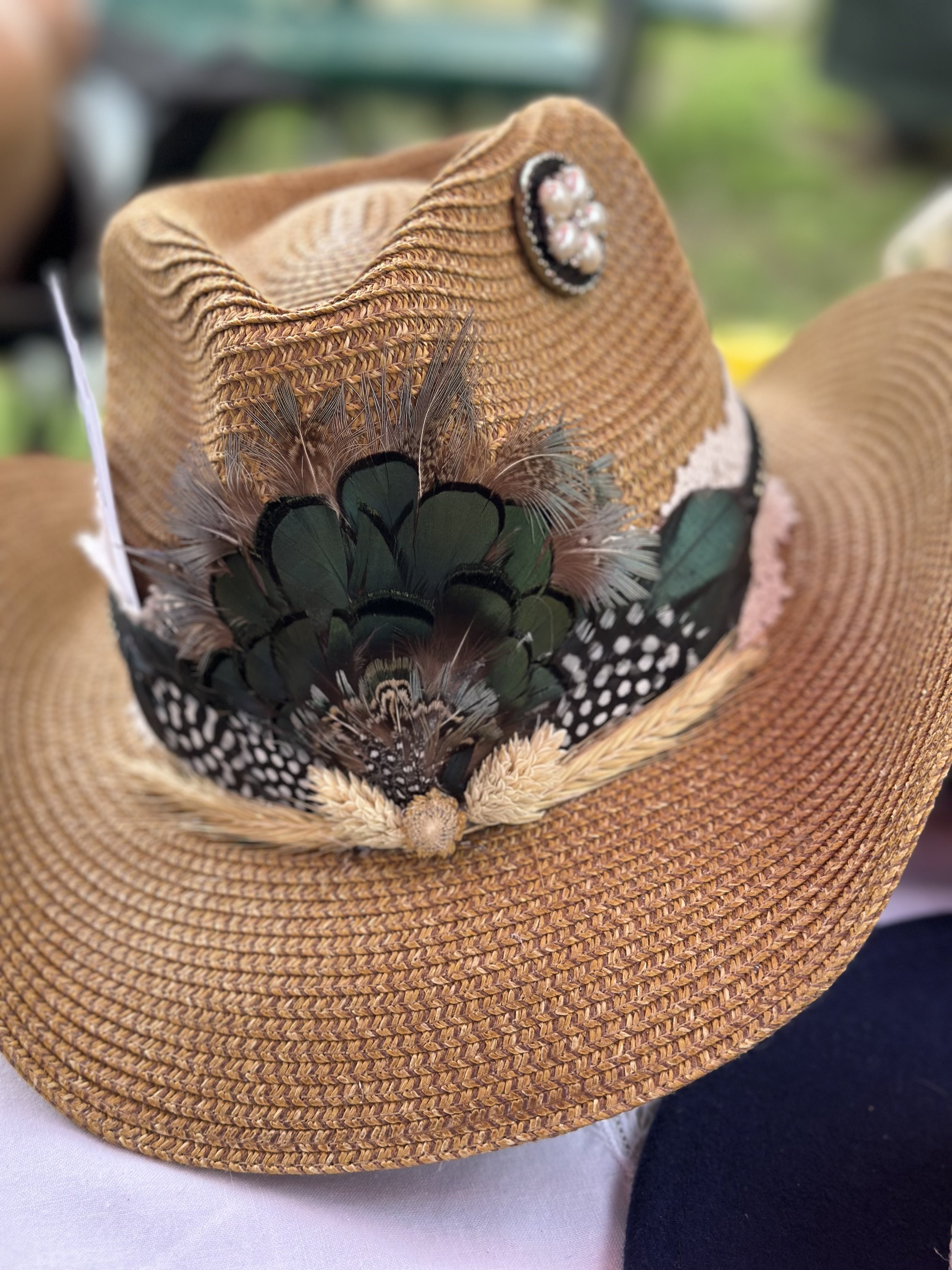 A brown wide-brimmed straw hat decorated with colorful feathers, pearls, flowers, and black and white polka dots.