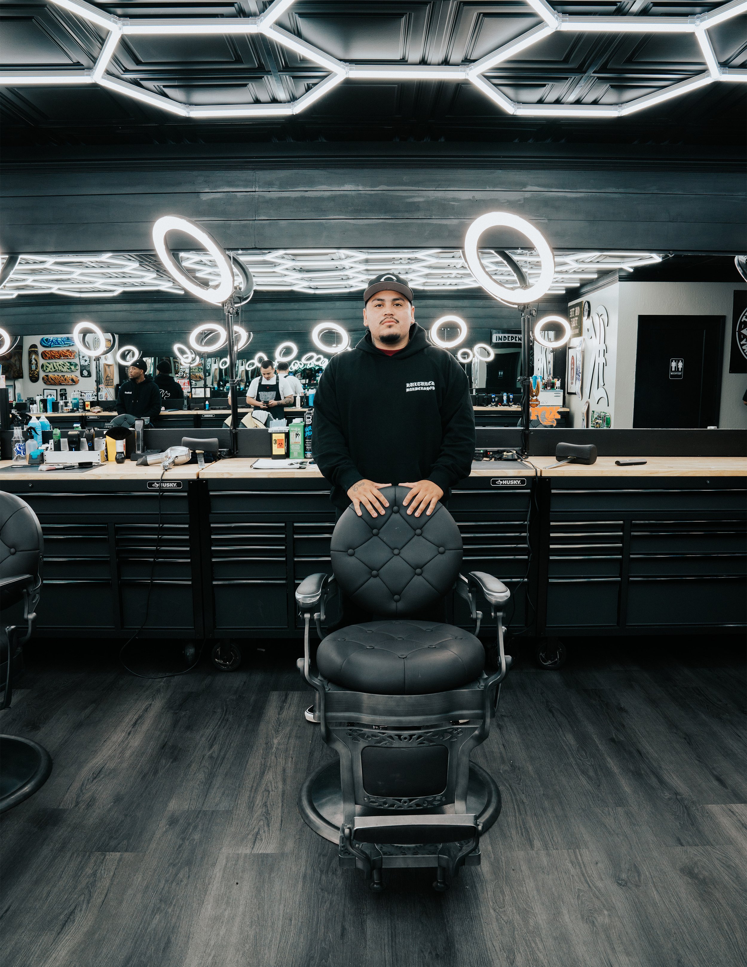 Barber cutting a client's hair in a modern barber shop with ring lights and mirrors.