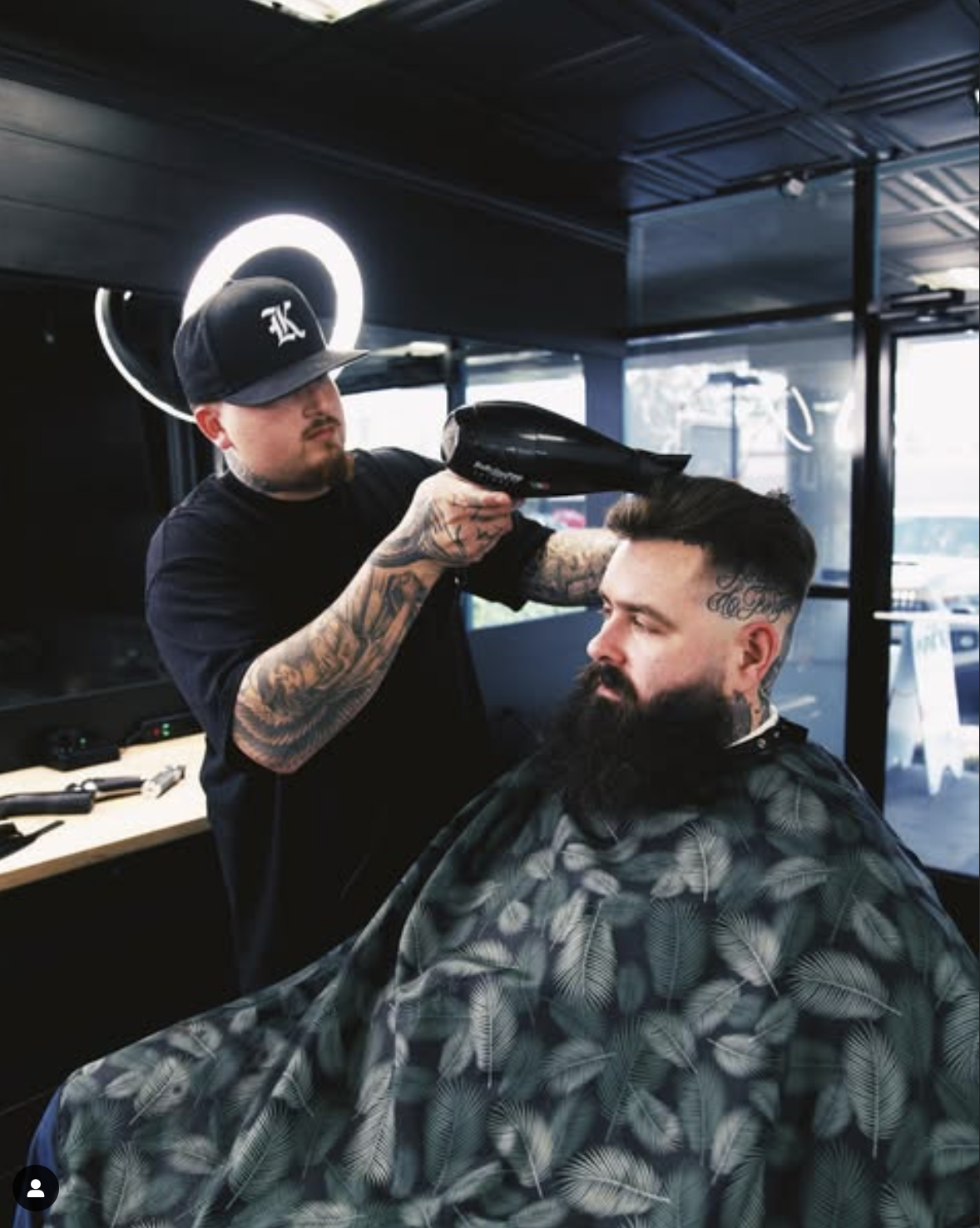 Barber styling bearded man's hair with blow dryer in modern barber shop.