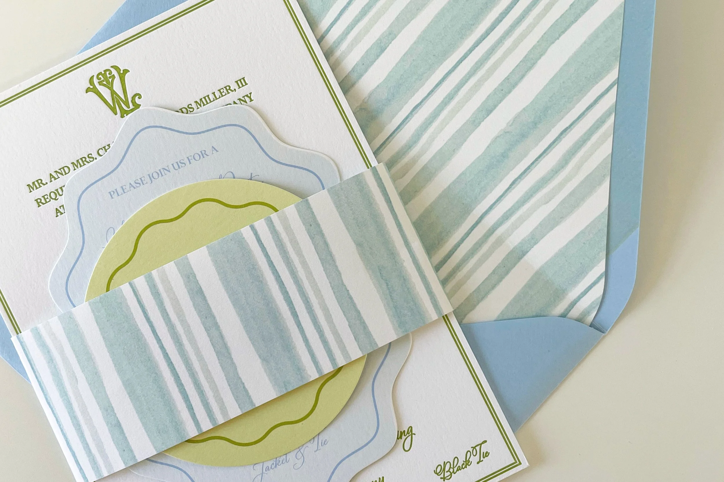 Invitation cards in pastel colors with striped paper band, positioned inside a light blue envelope.