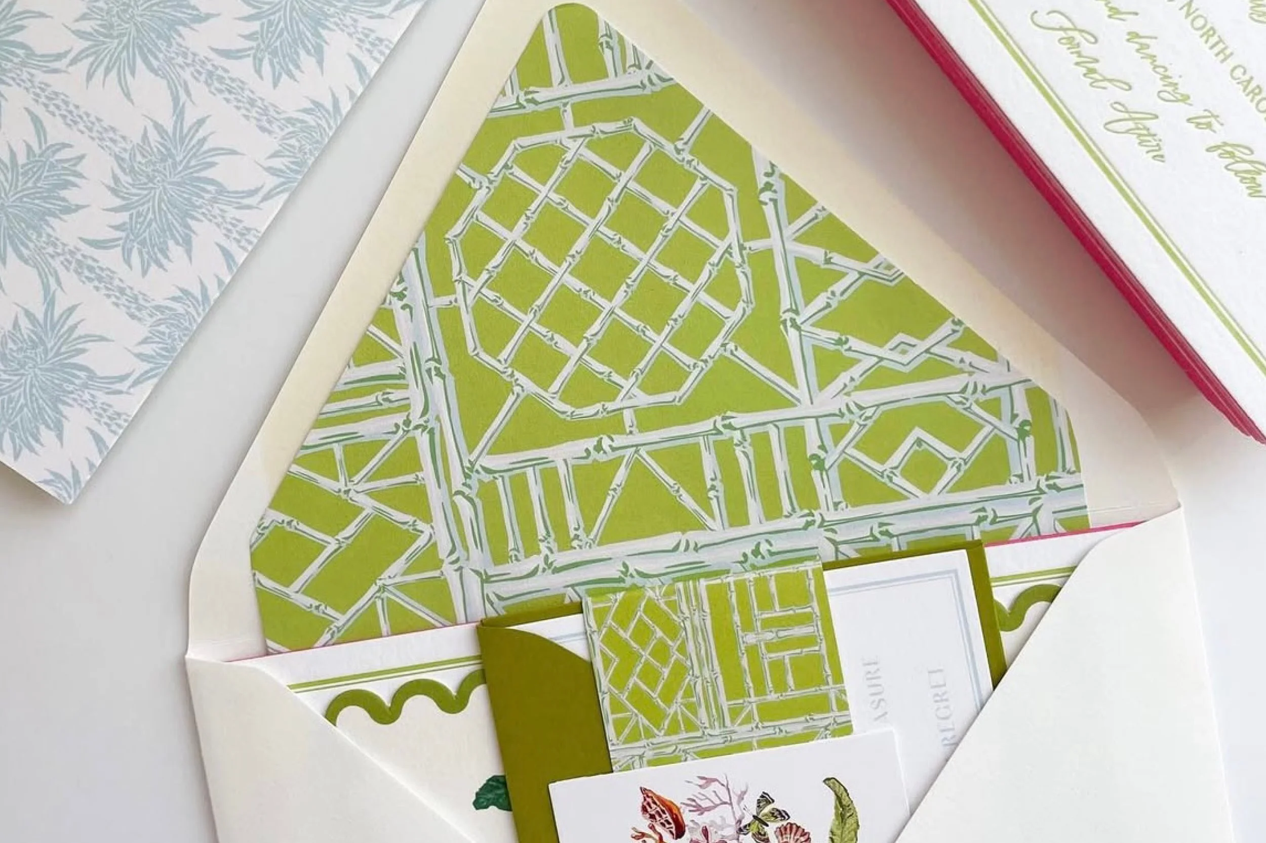 Open invitation envelope with green and white patterned interior, containing a card and a small matching paper note.