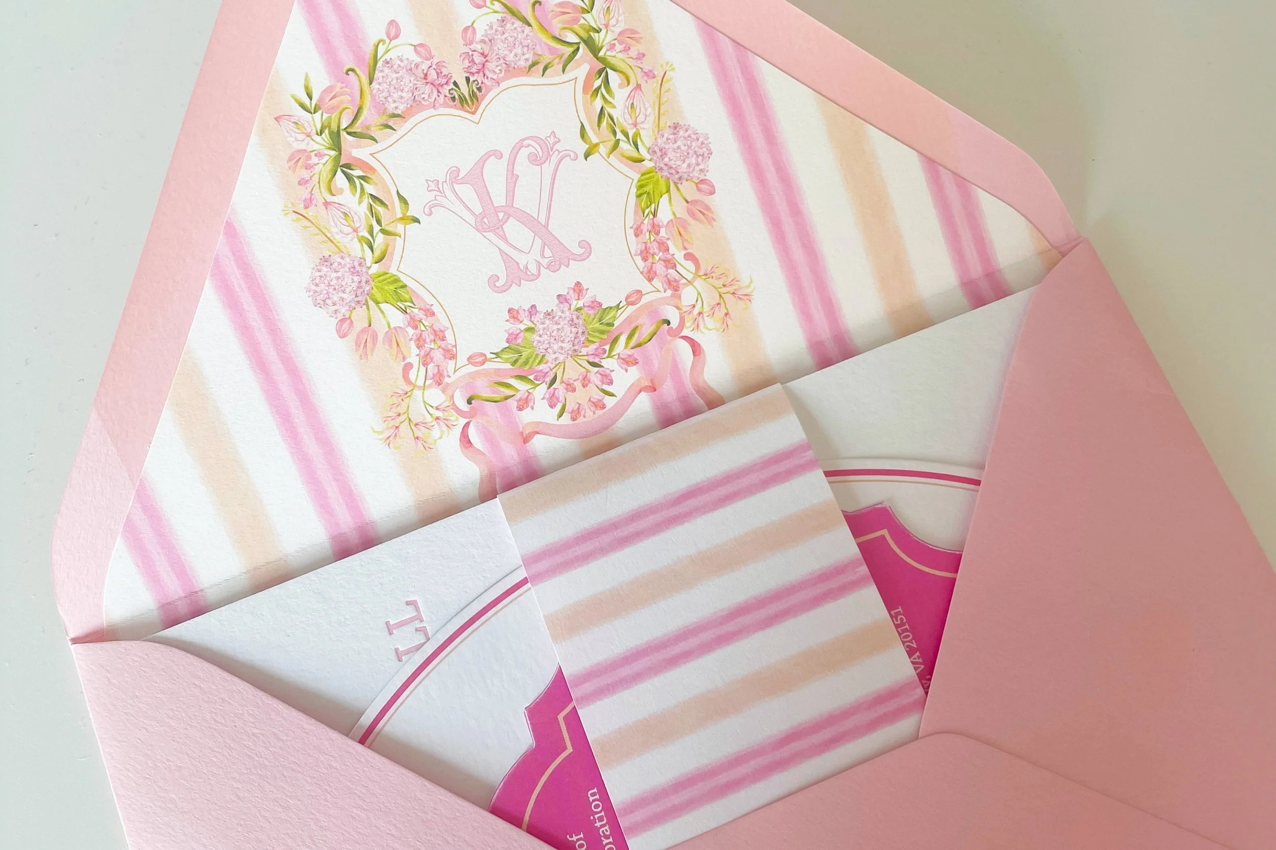 A sunset color pink wedding invitation suite with a watercolor crest monogram design inside, envelope liner.