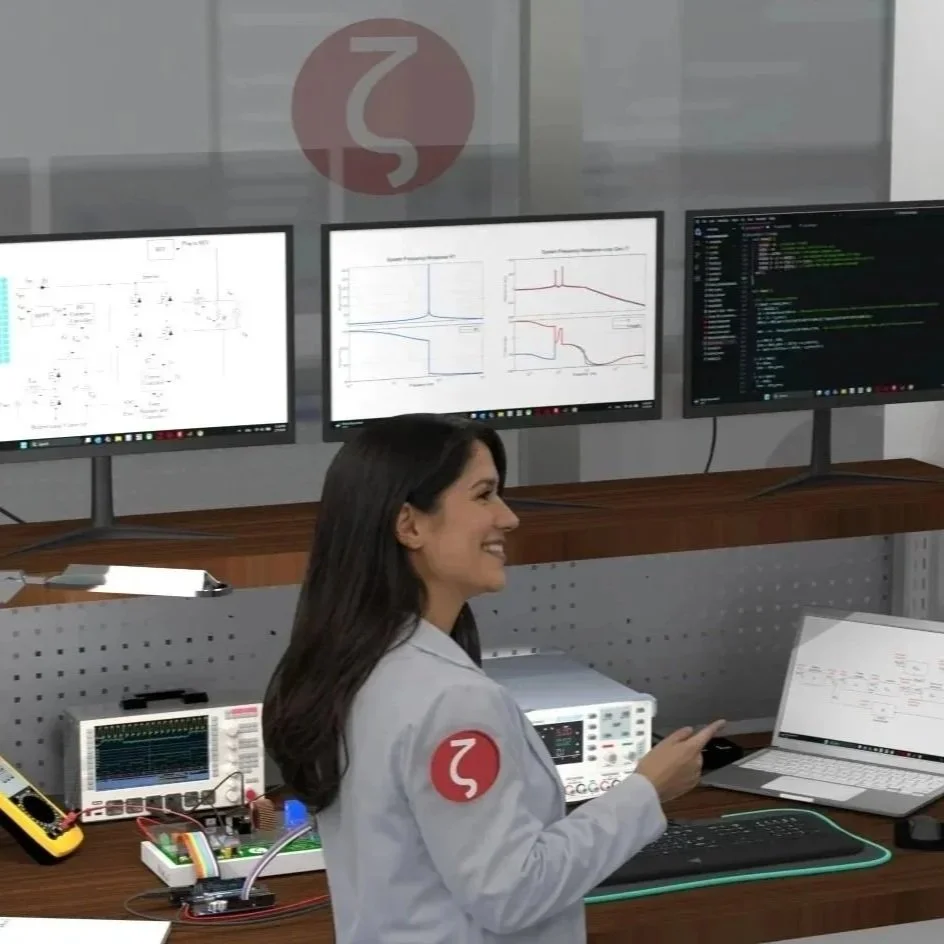 A woman working at a technical lab with multiple computer monitors, test equipment, and electronic components, smiling while looking at her laptop.