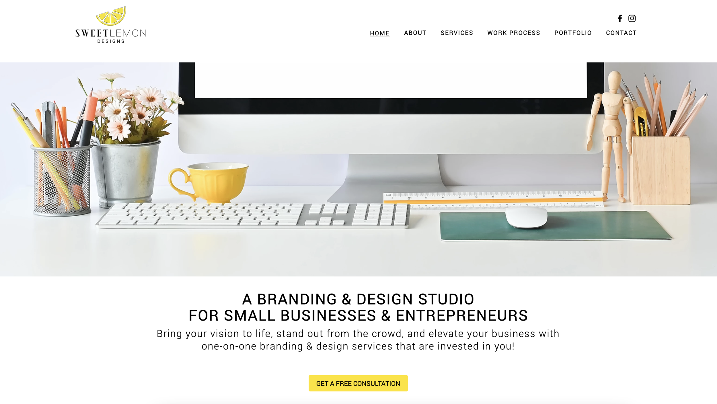 A clean, organized workspace with a computer monitor, keyboard, mouse, yellow cup, and various office supplies such as pens, pencils, and a small wooden mannequin. There are decorative elements like a potted plant and a flower arrangement.