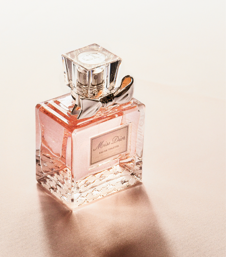A bottle of Miss Dior Eau de Parfum with a silver bow on the cap, placed on a light-colored surface.