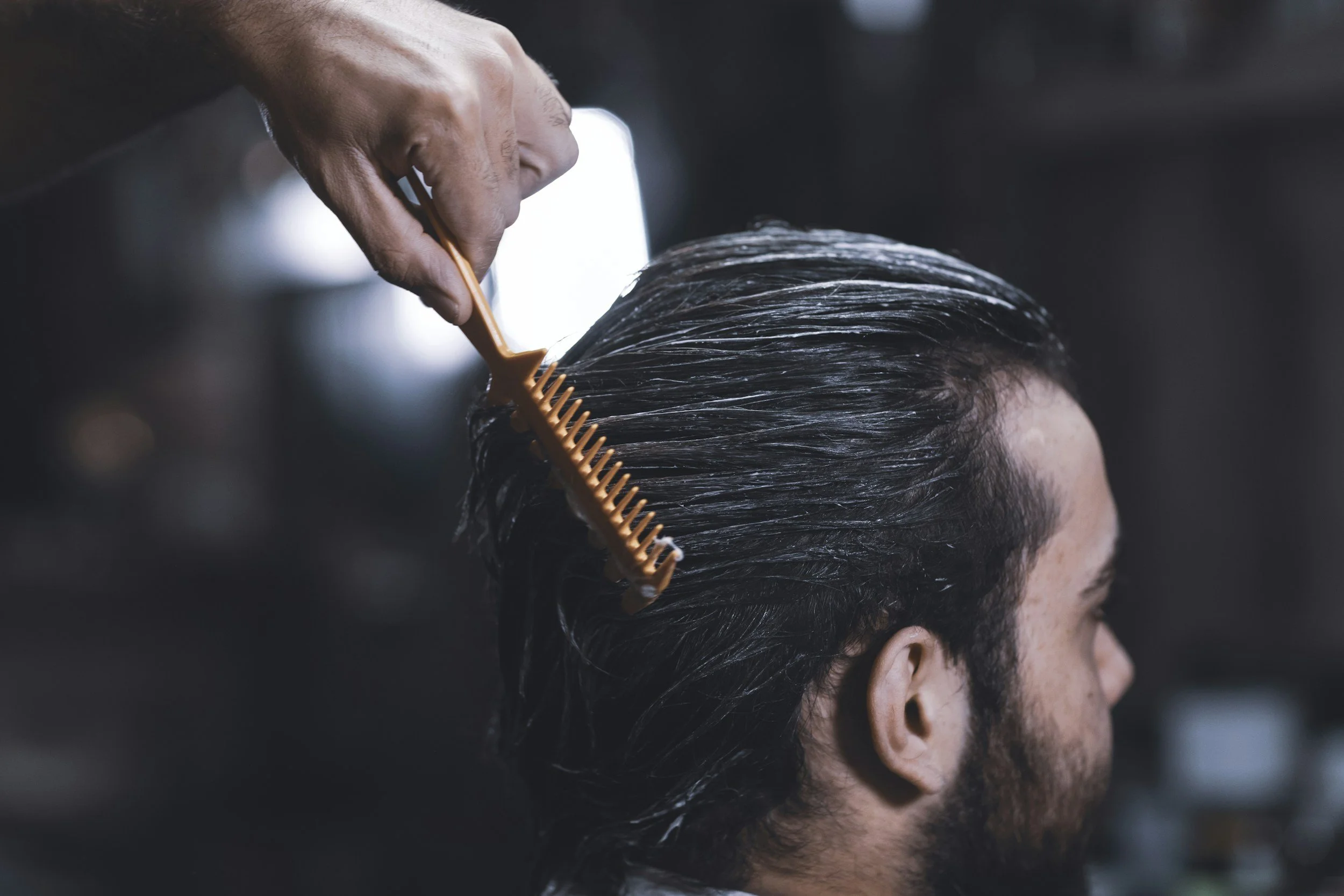 A man getting a haircut, with hair being combed back and a comb in the hair.