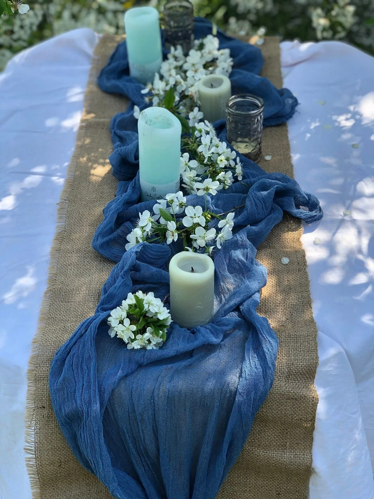 Blue cheesecloth table runner with candles and white floral accents on wooden table, romantic wedding table decor in Portland Oregon