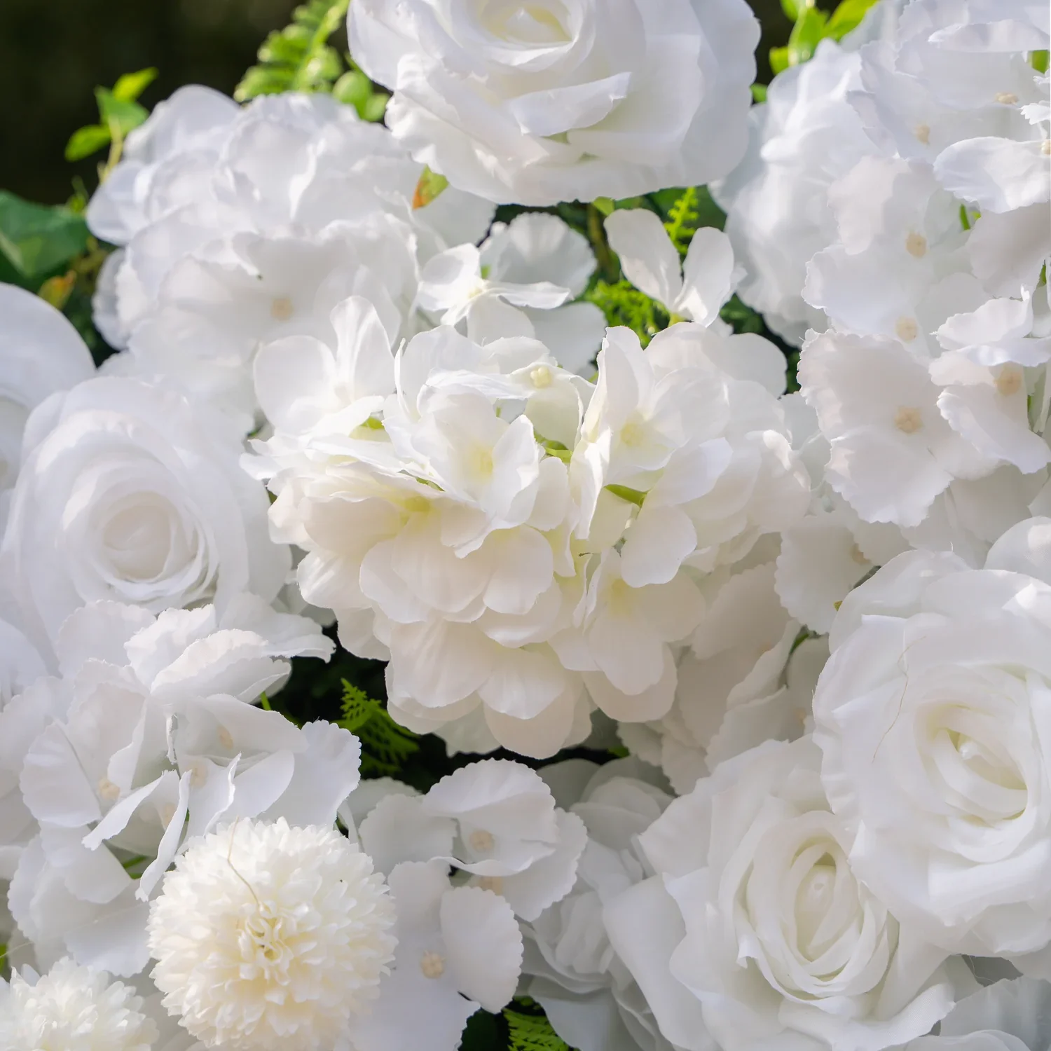 Elegant white rose flower wall backdrop with warm uplighting, surrounded by gold stands, candle clusters, and soft draped fabric beneath a crystal chandelier — a romantic luxury wedding photo backdrop.