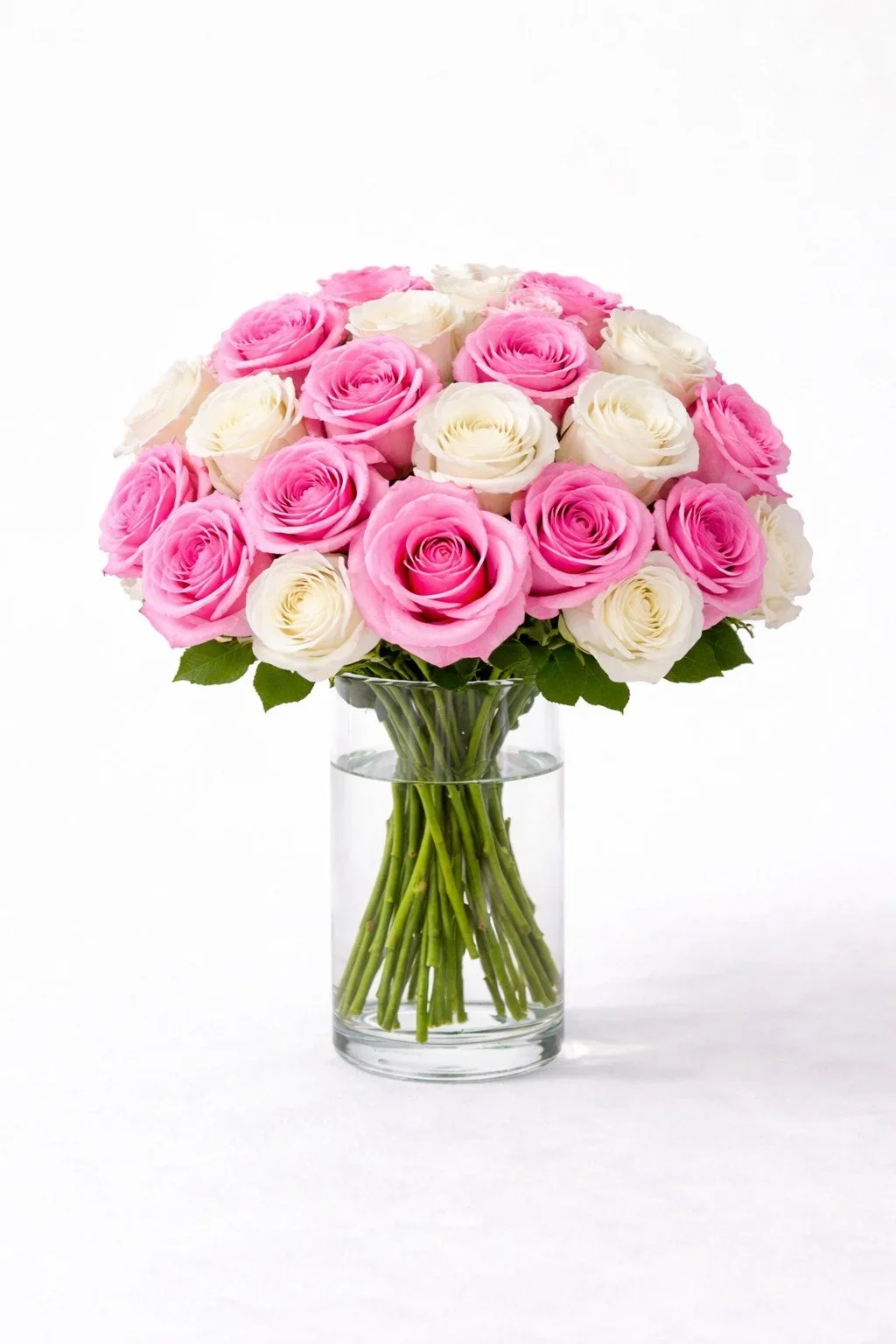 Realistic artificial long stem pink and white roses arranged in a clear glass cylinder vase.