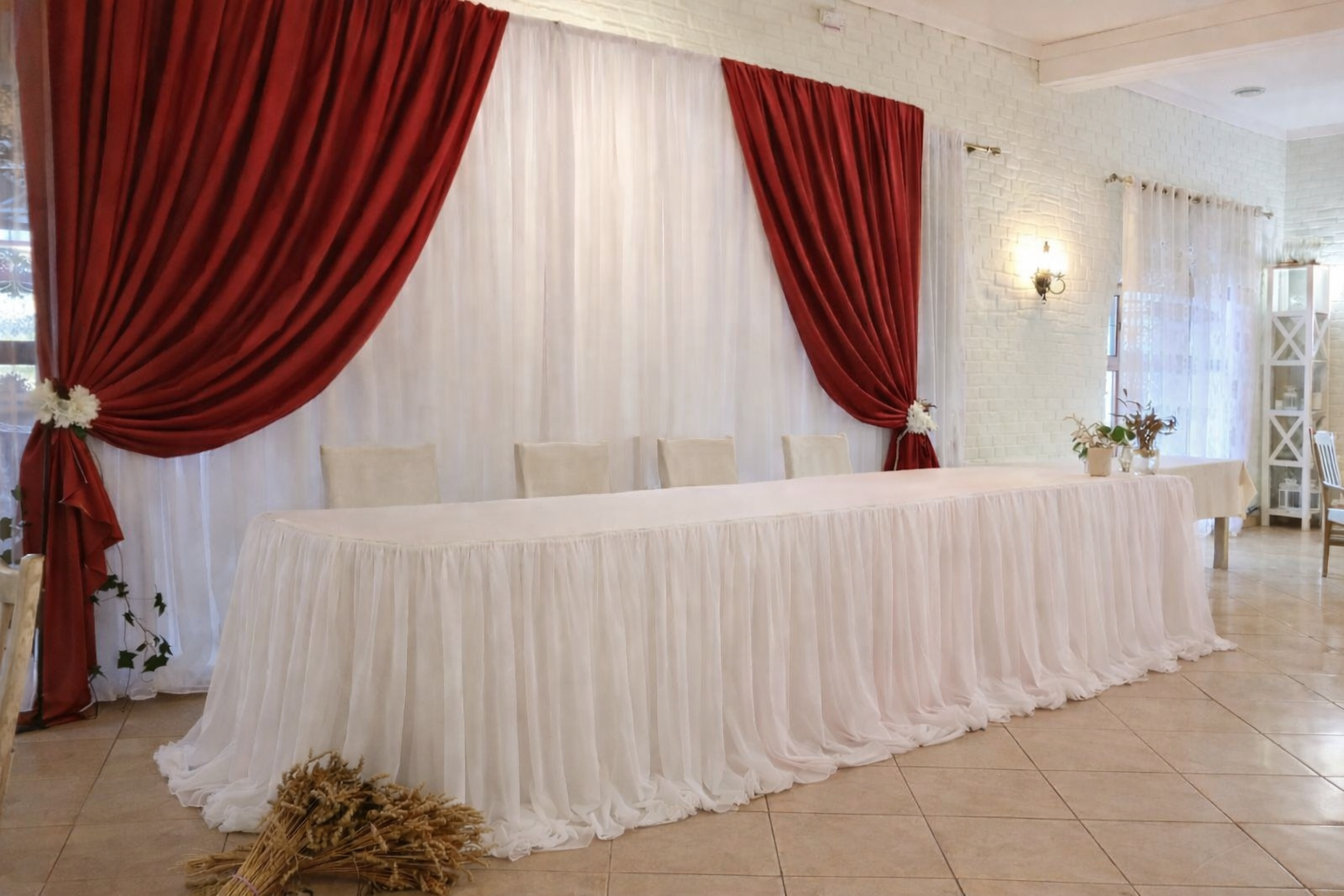 Elegant sweetheart head table with white draping and bold red backdrop curtains, minimal decor setup for wedding reception staging.