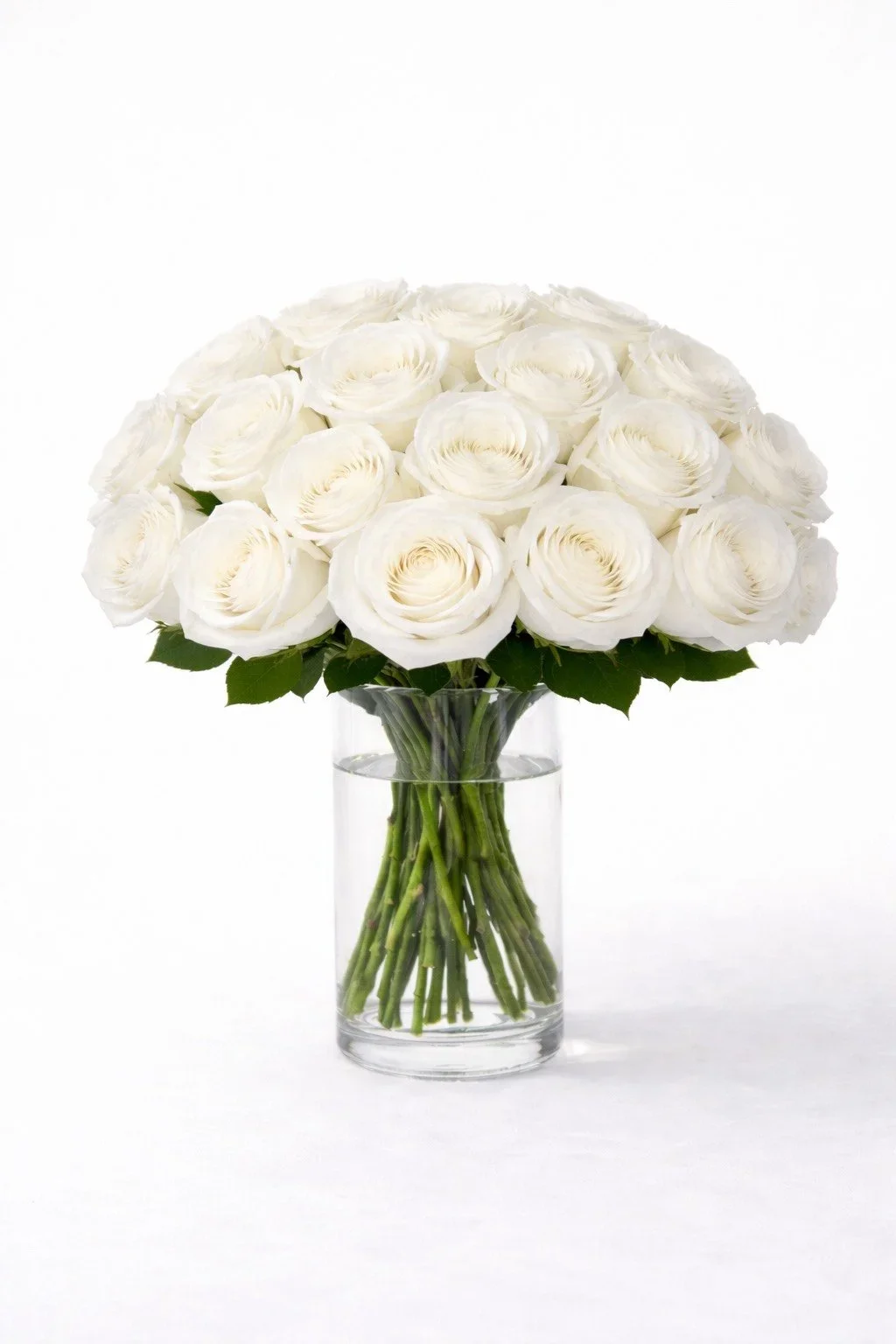 Realistic artificial long stem white roses arranged in a clear glass cylinder vase.