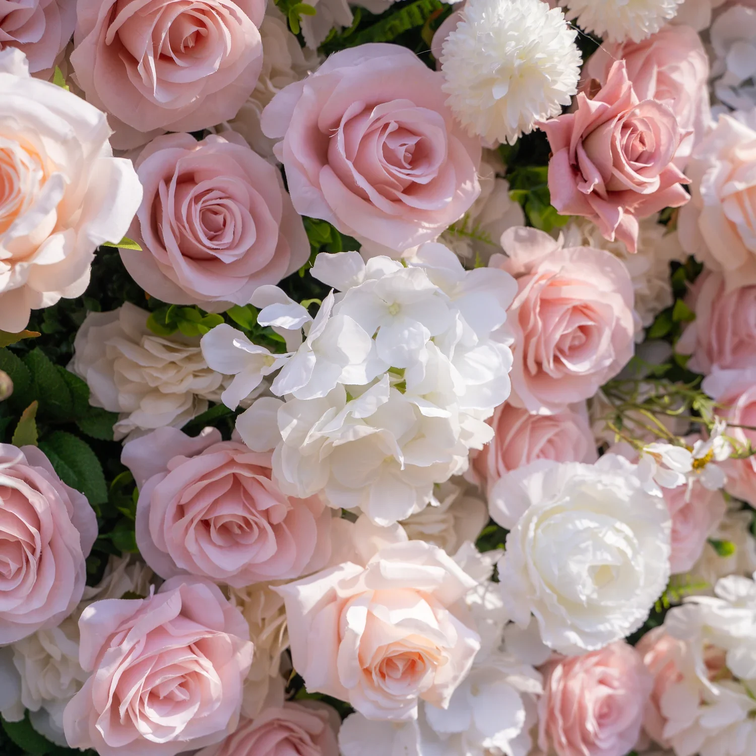 Blush pink and white rose flower wall backdrop set outdoors on a grassy lawn, with soft sunset sky, trees, and distant mountains in the background — perfect for weddings or photo booths.