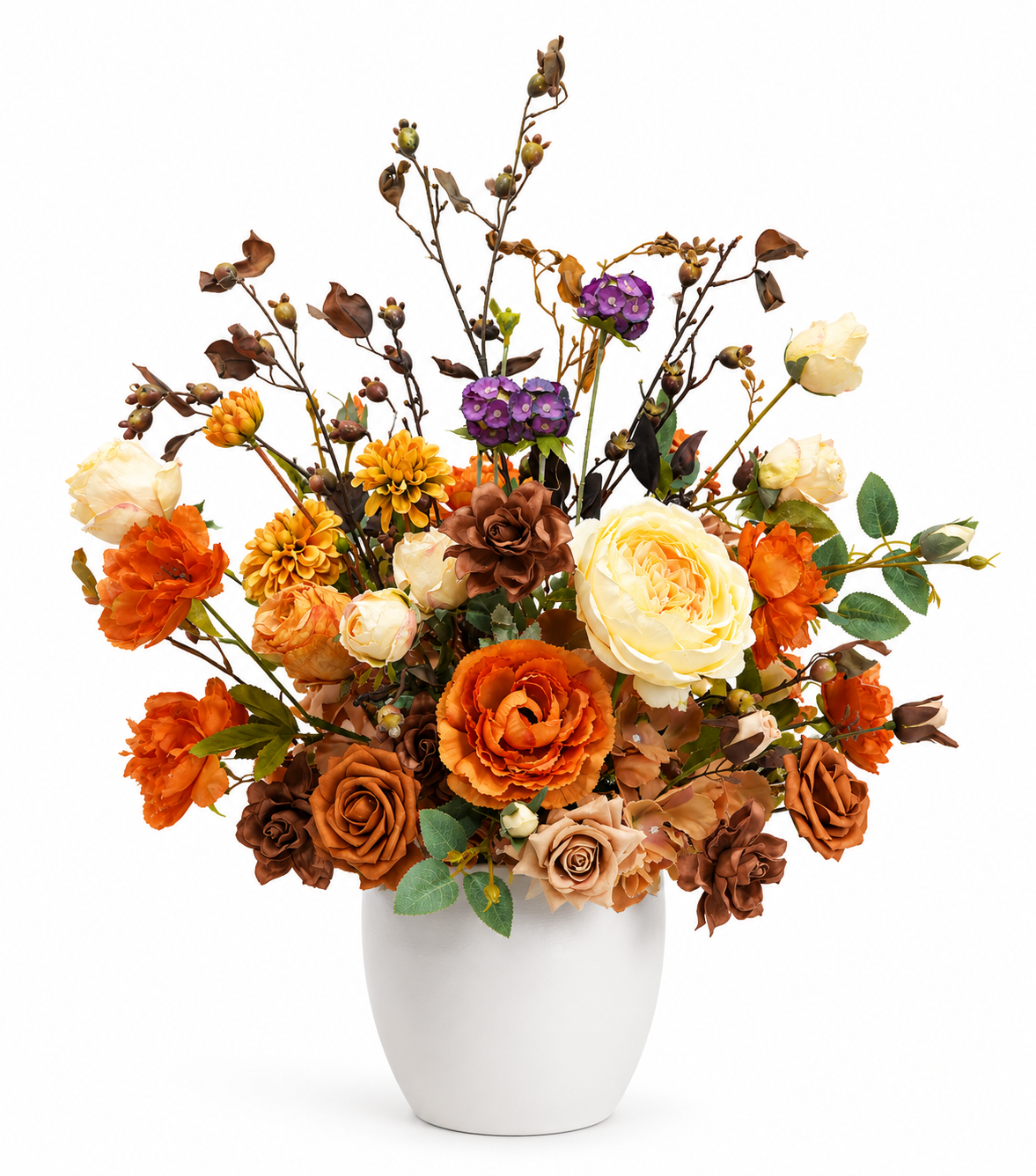 Artificial fall floral arrangement with orange, ivory, brown, and purple flowers with decorative branches in a white ceramic vase on a white background.