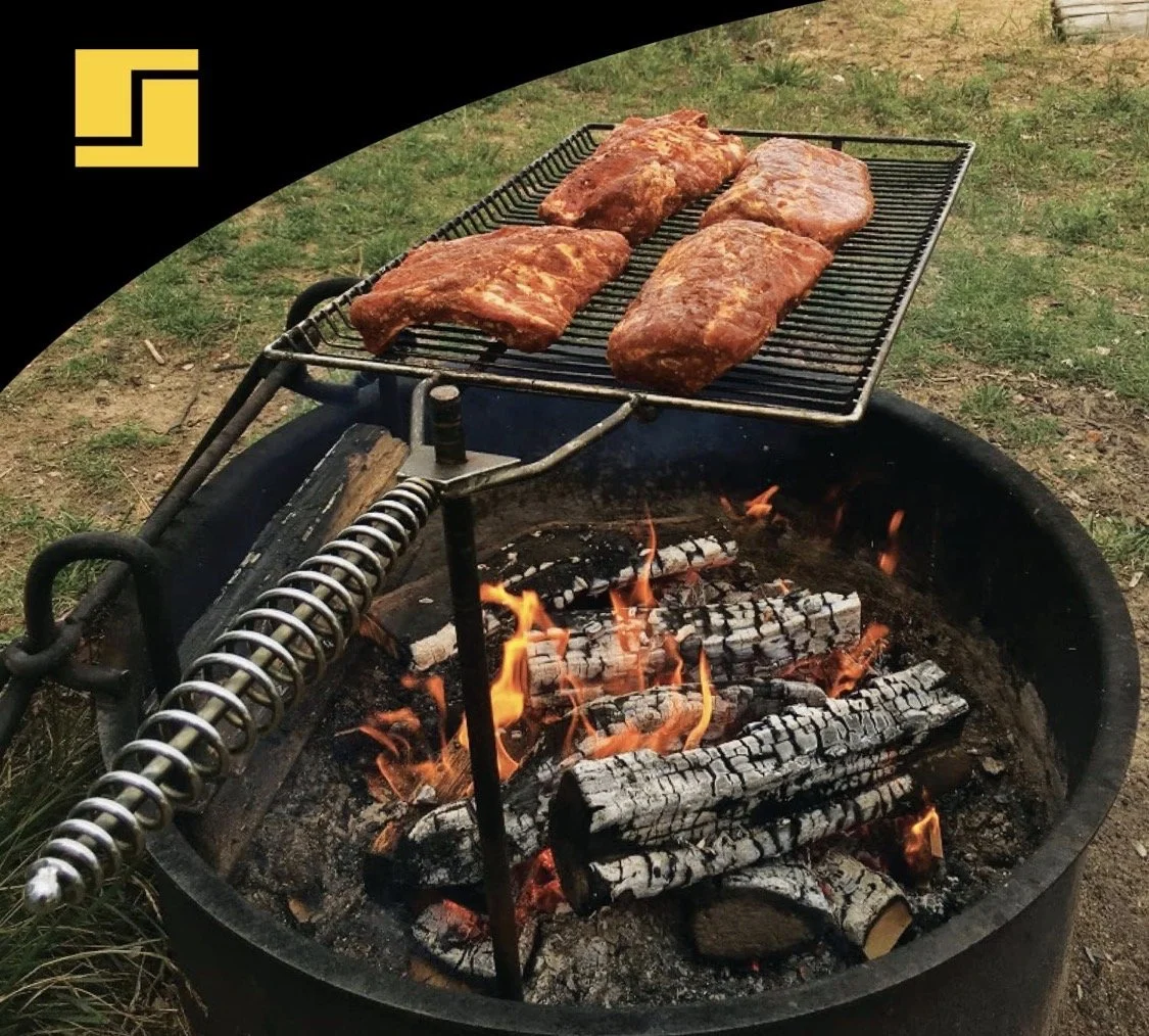adjustable campfire grill grate with swivel arm cooking meat over open fire pit with burning logs