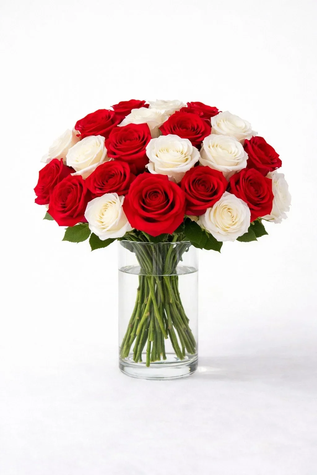 Realistic artificial long stem red and white roses arranged in a clear glass cylinder vase.