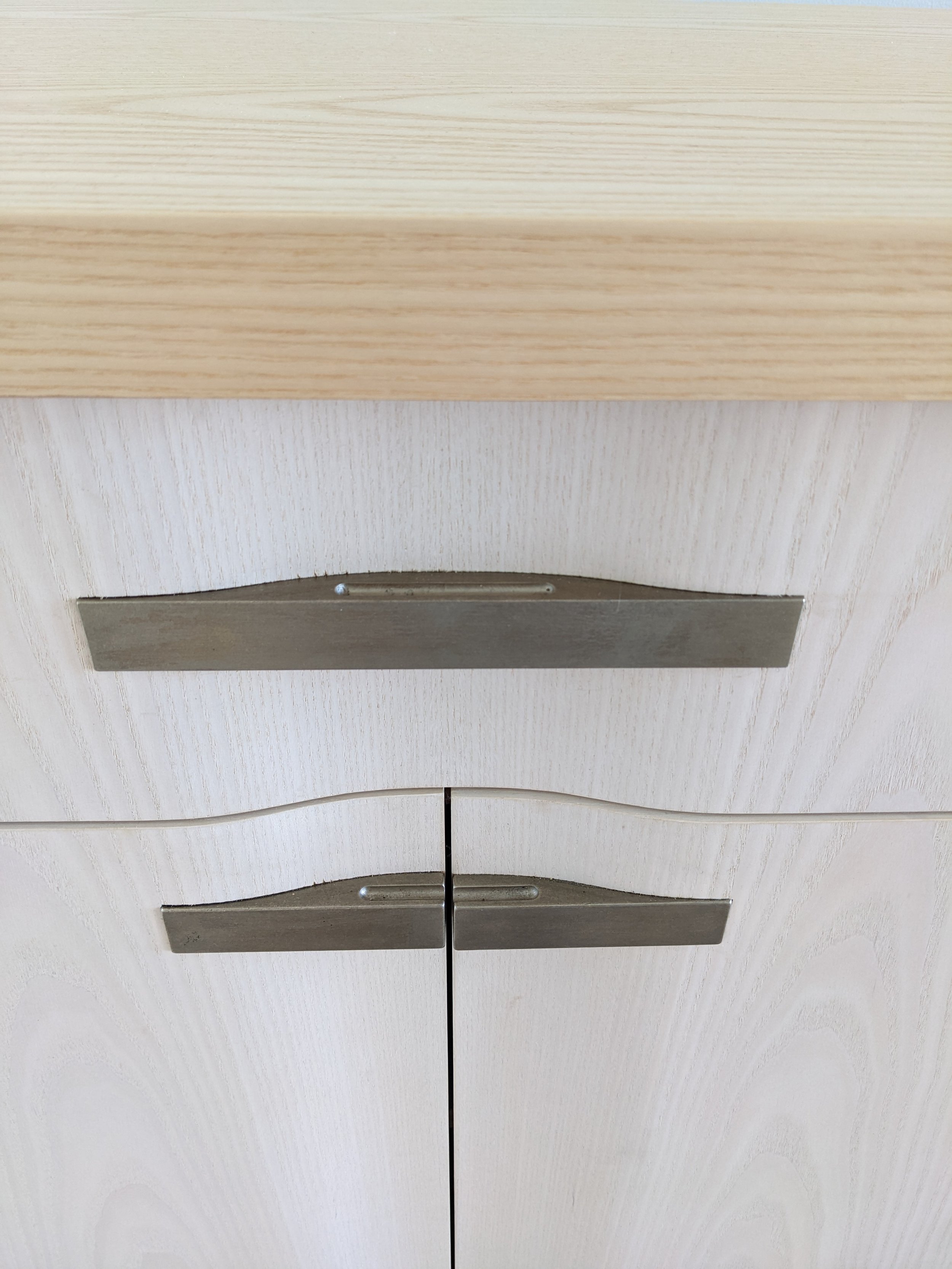 Close-up of a light-colored wooden cabinet with horizontal metal handles.
