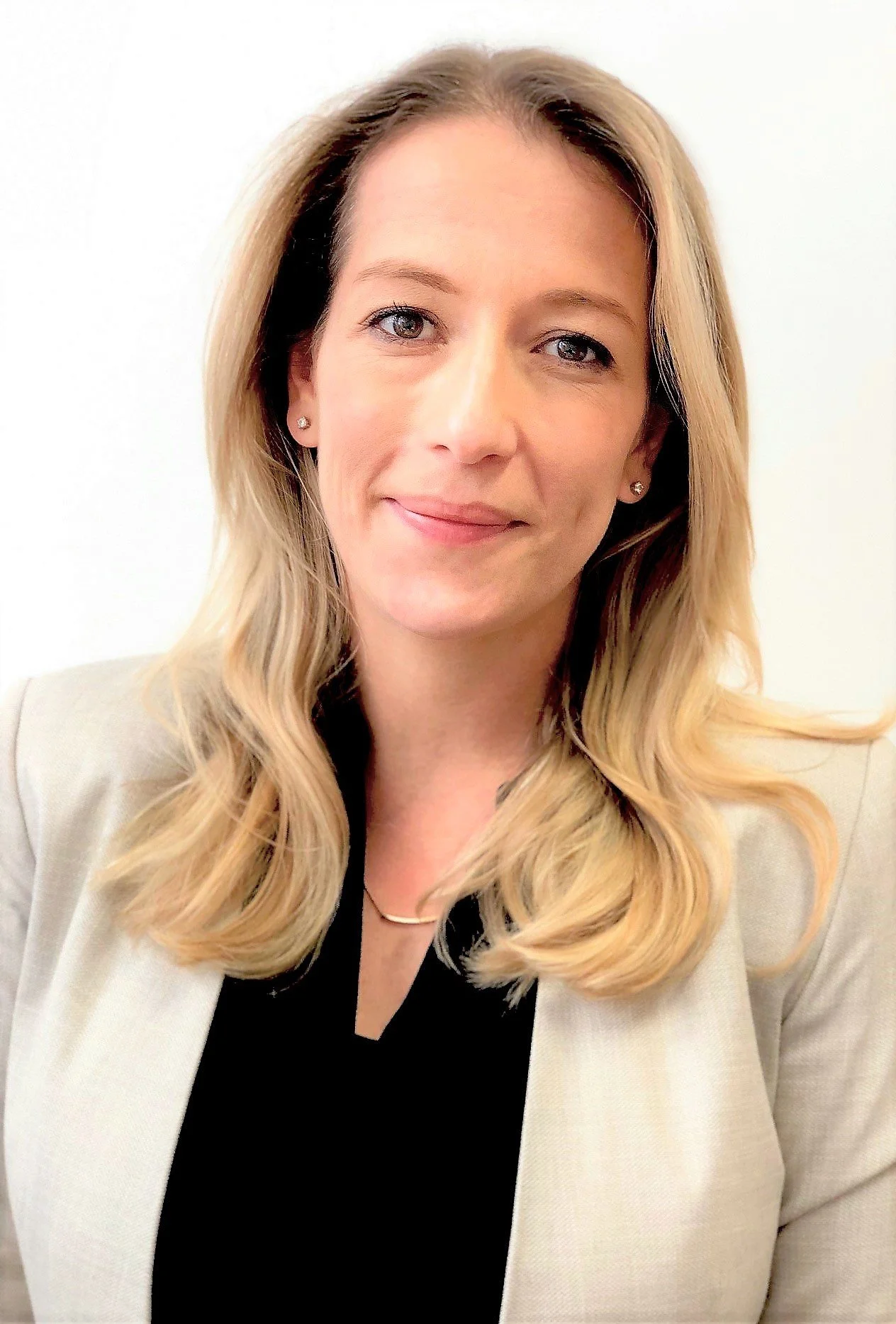 A professional woman with blonde, wavy hair, light skin, wearing a cream blazer and black top, smiling softly, against a plain white background.