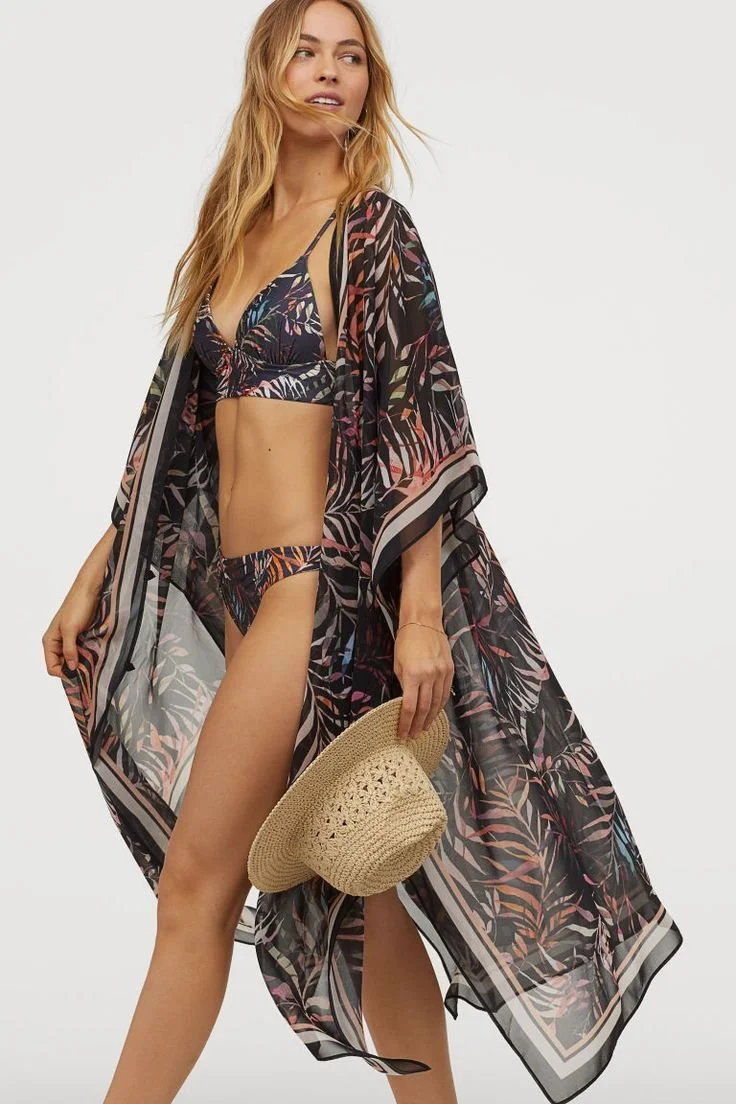 H&M lookbook editorial,  a woman in a tropical floral bikini and a sheer, patterned maxi kaftan cover-up, both by EllaJo Studio holding a straw sunhat.