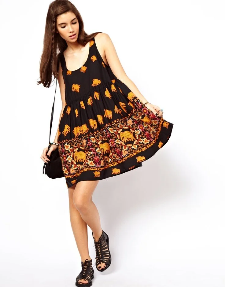 Young woman wearing a black dress with orange elephant and floral patterns, posing against a plain white background.