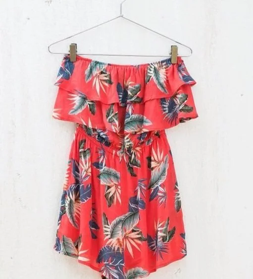 Red off-the-shoulder floral dress hanging on a hanger against a white wall.