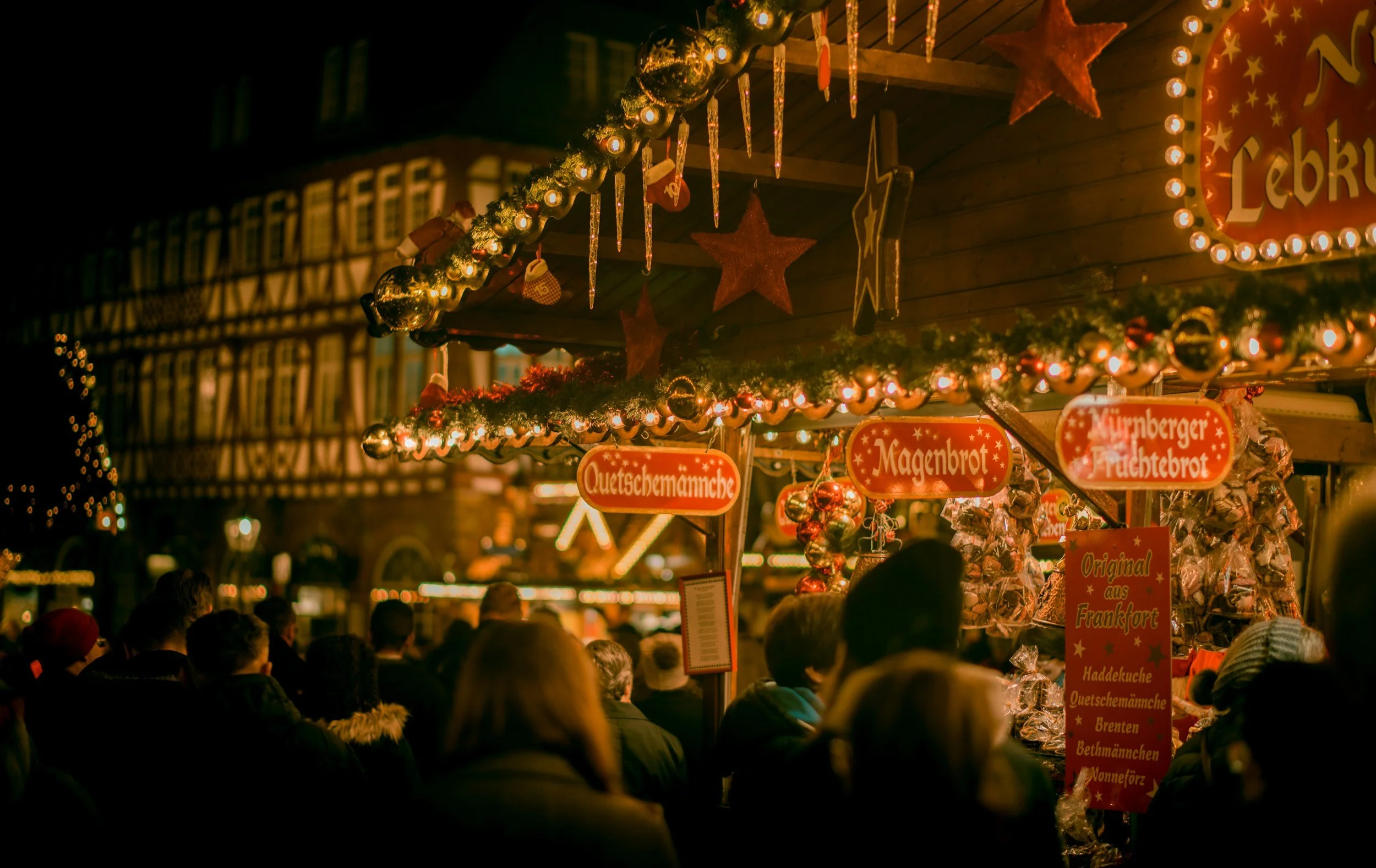 Nighttime at a well-lit Christmas market with stall signs in German.