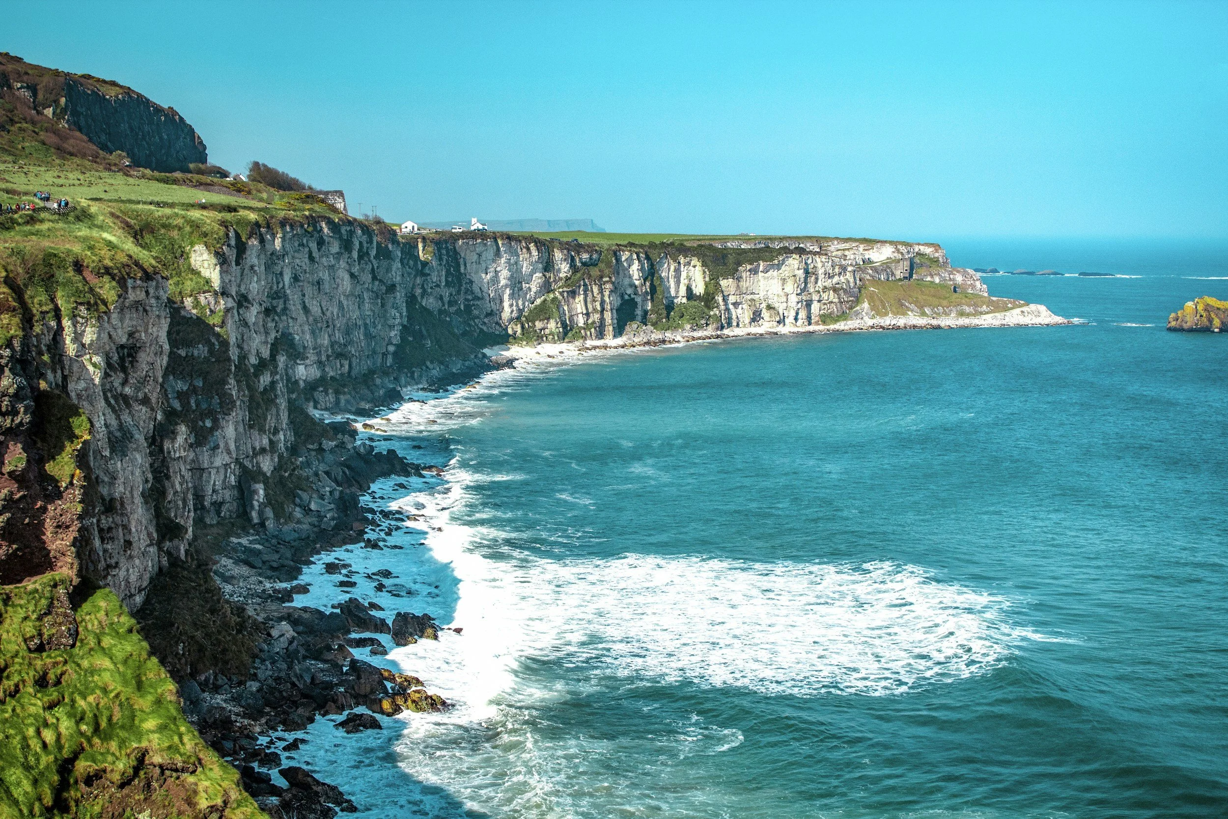 Stark white cliffs on the left end in blue waters and blue skies.