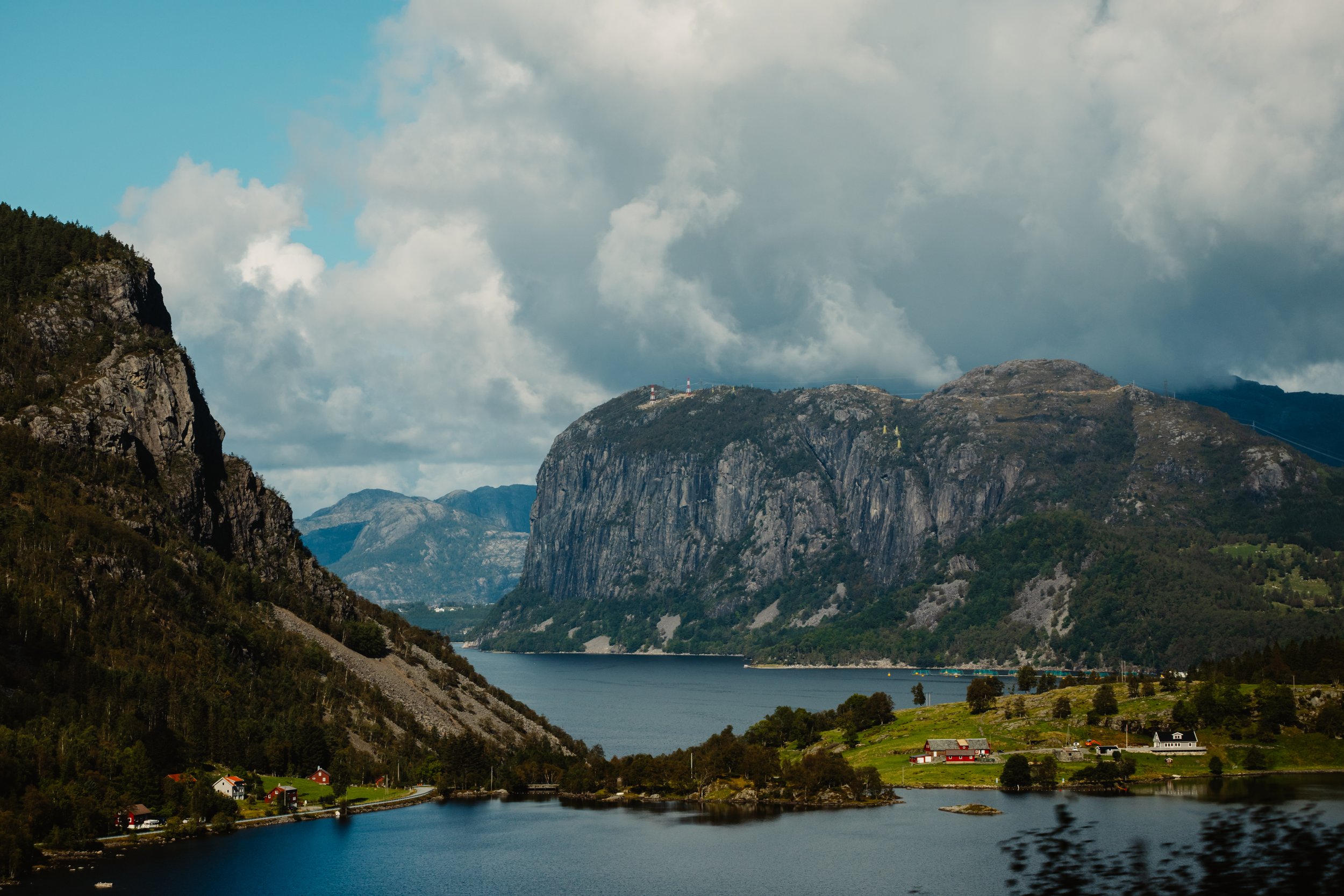 Scenic view of cliffs and fjord with small houses and greenery.
