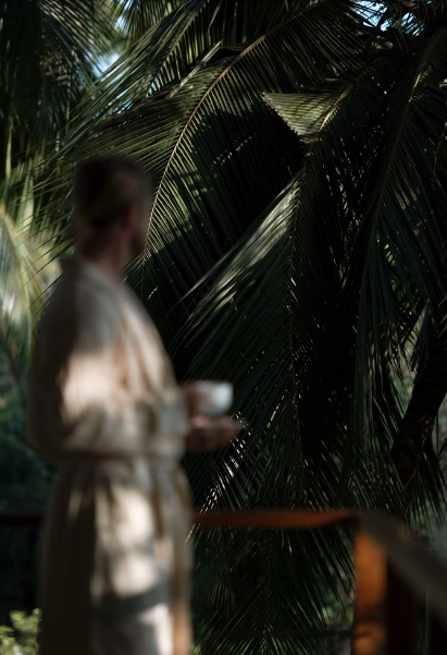 A woman holding a bowl, standing outdoors near large tropical palm leaves.