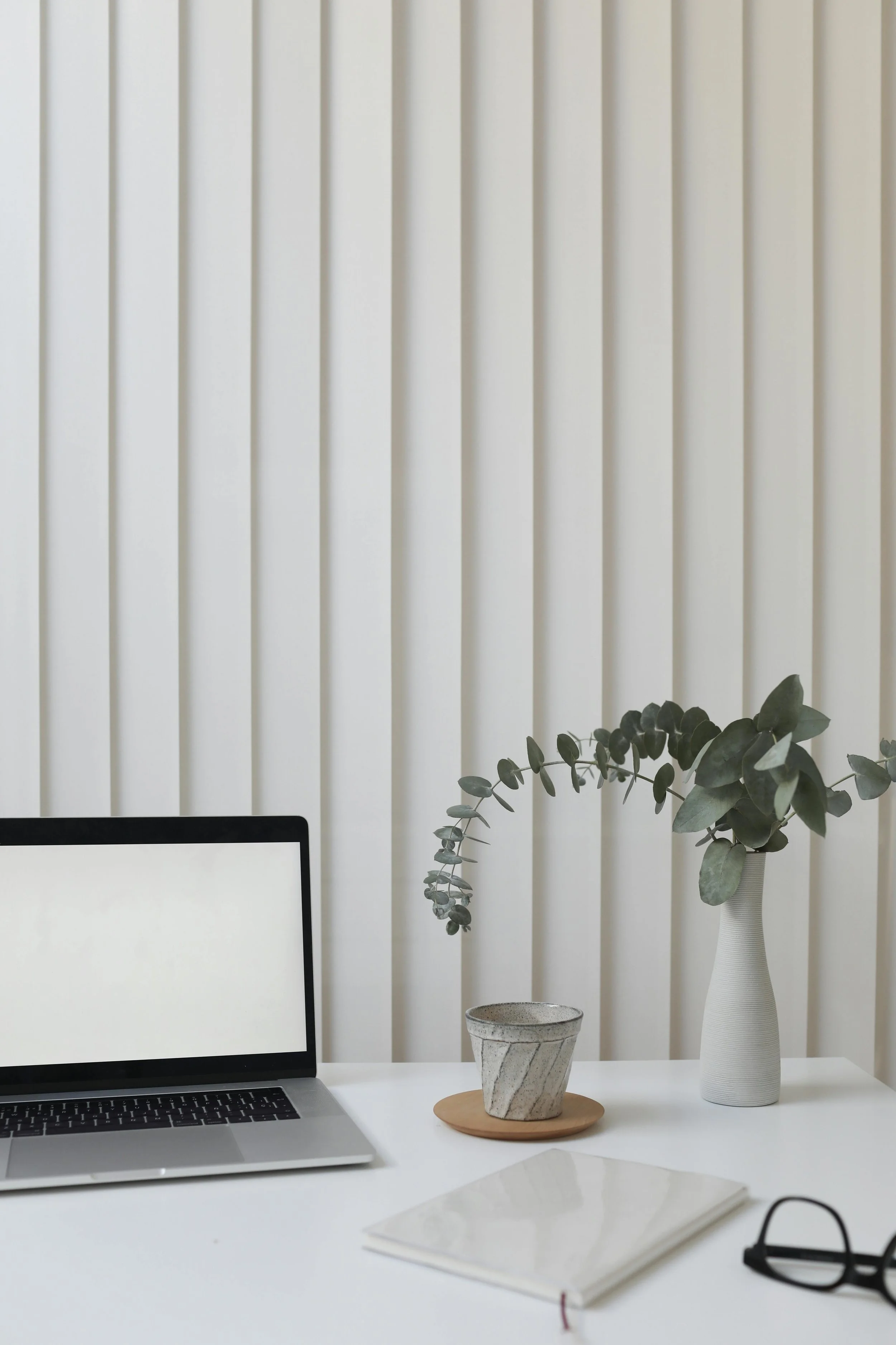 laptop on desk with eucalyptus in vase