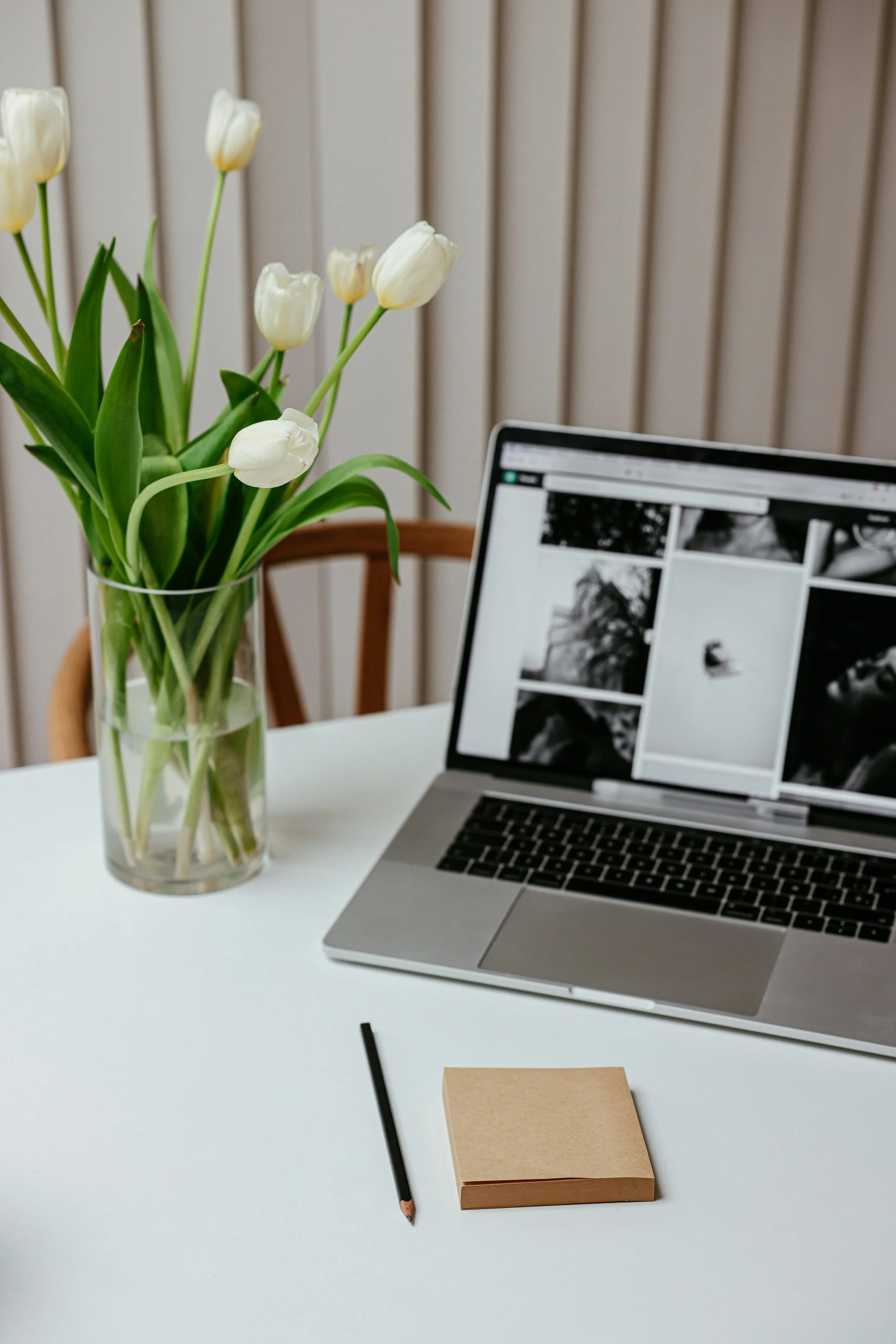 mac book on a desk next to a vase with white tulips