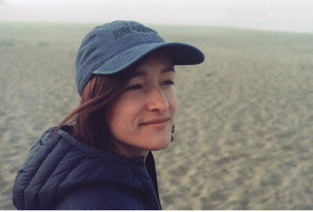 woman wearing blue jumper and blue cap with beach in the backgound