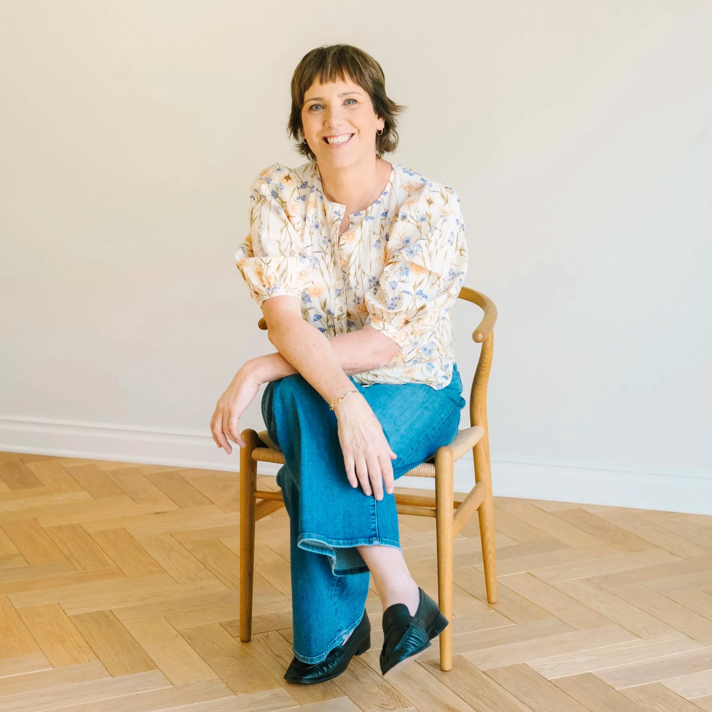 woman wearing blue jeans and floral shirt sitting on a chair