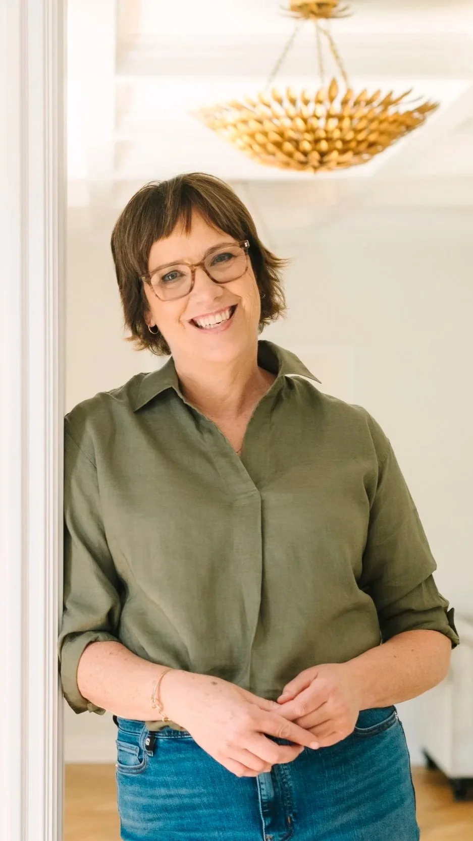 woman wearing green shirt leaning against door frame wearing brown glasses and brown hair