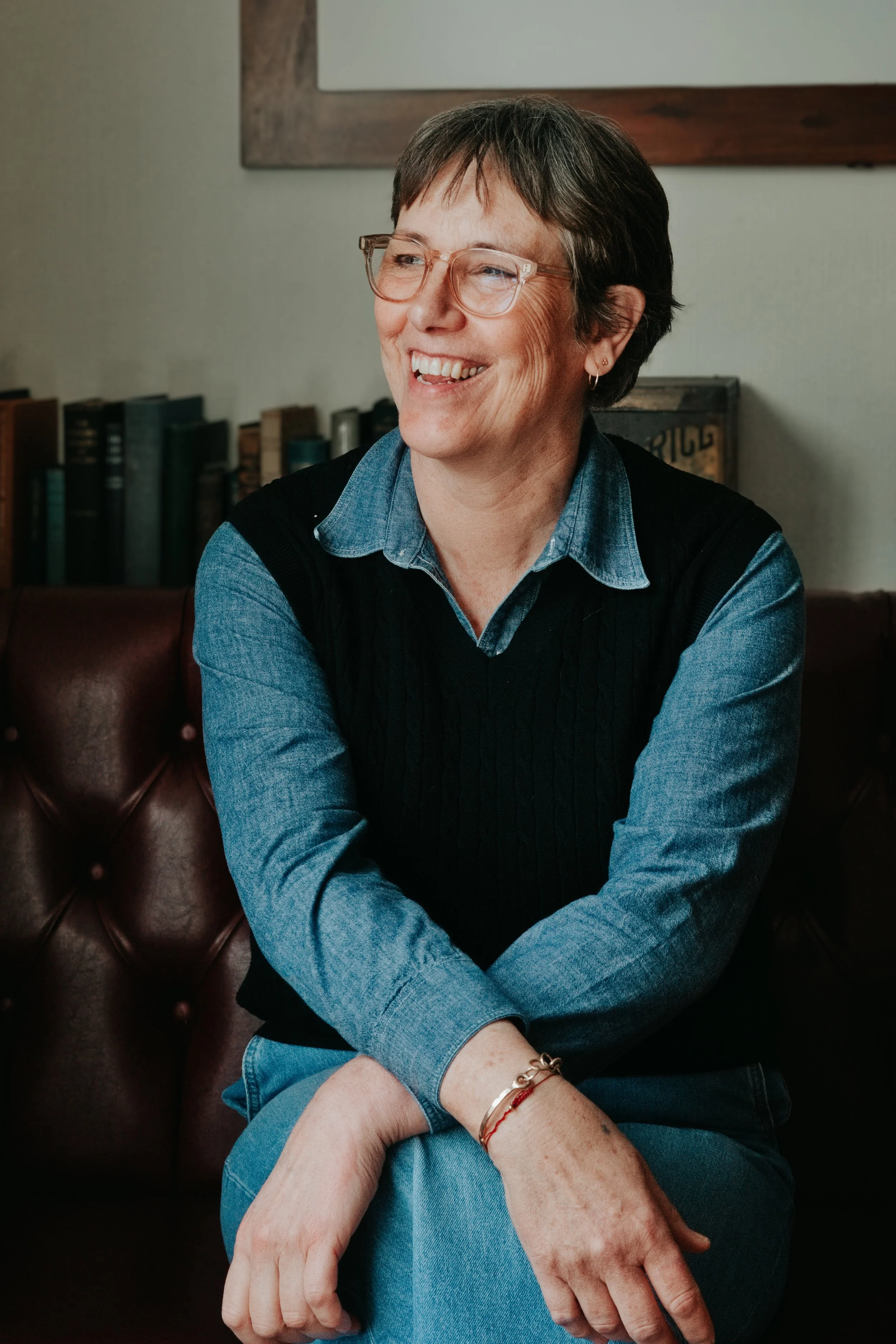 woman laughing wearing glasses and denim shirt and black jumper